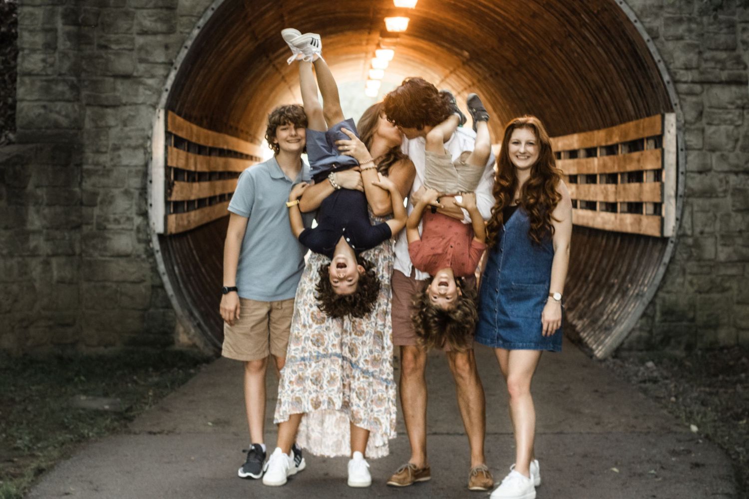 Parents kissing while holding their children upside down during a playful family photo session