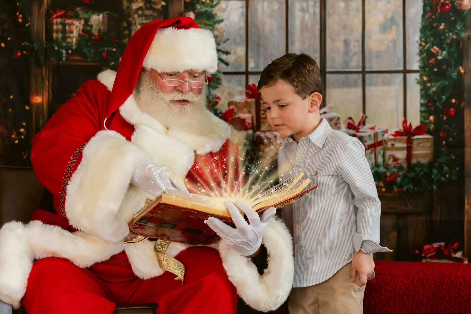 Santa Claus reading a glowing magical book with a young boy during a Christmas holiday photo session.