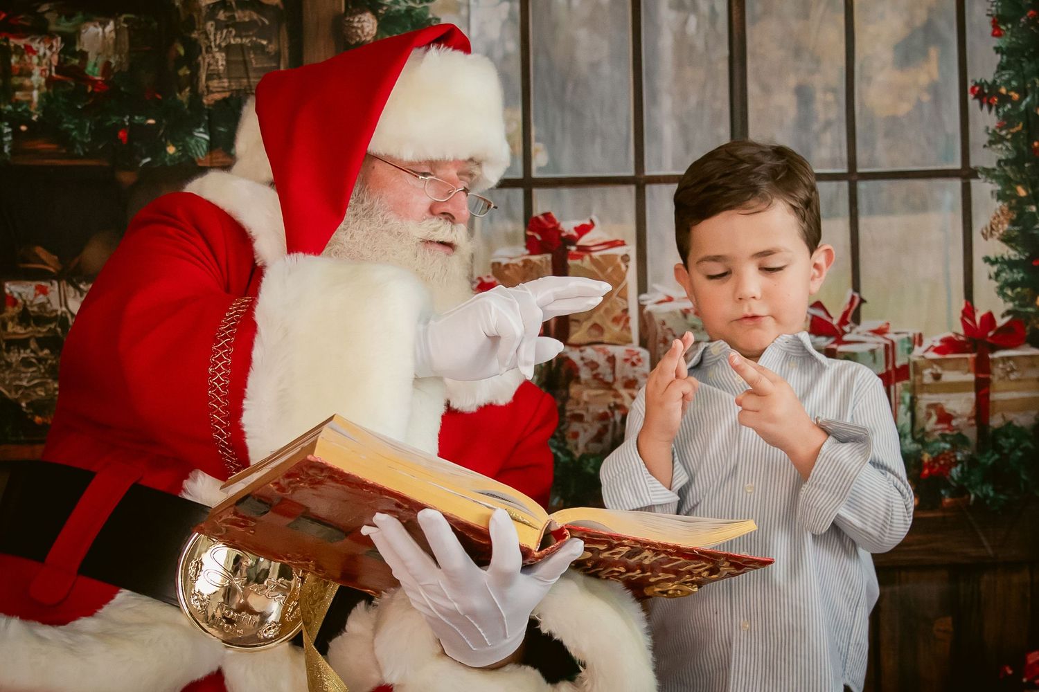 Santa Claus reads a Christmas book with a young boy surrounded by festive holiday decorations and gifts.