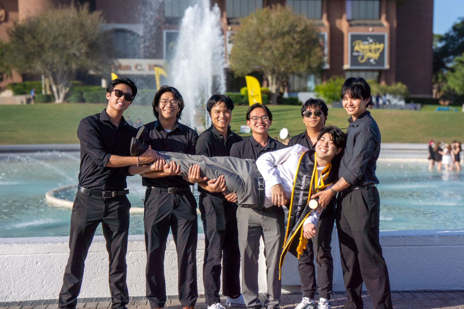 Group of graduates in dark attire posing by fountain.