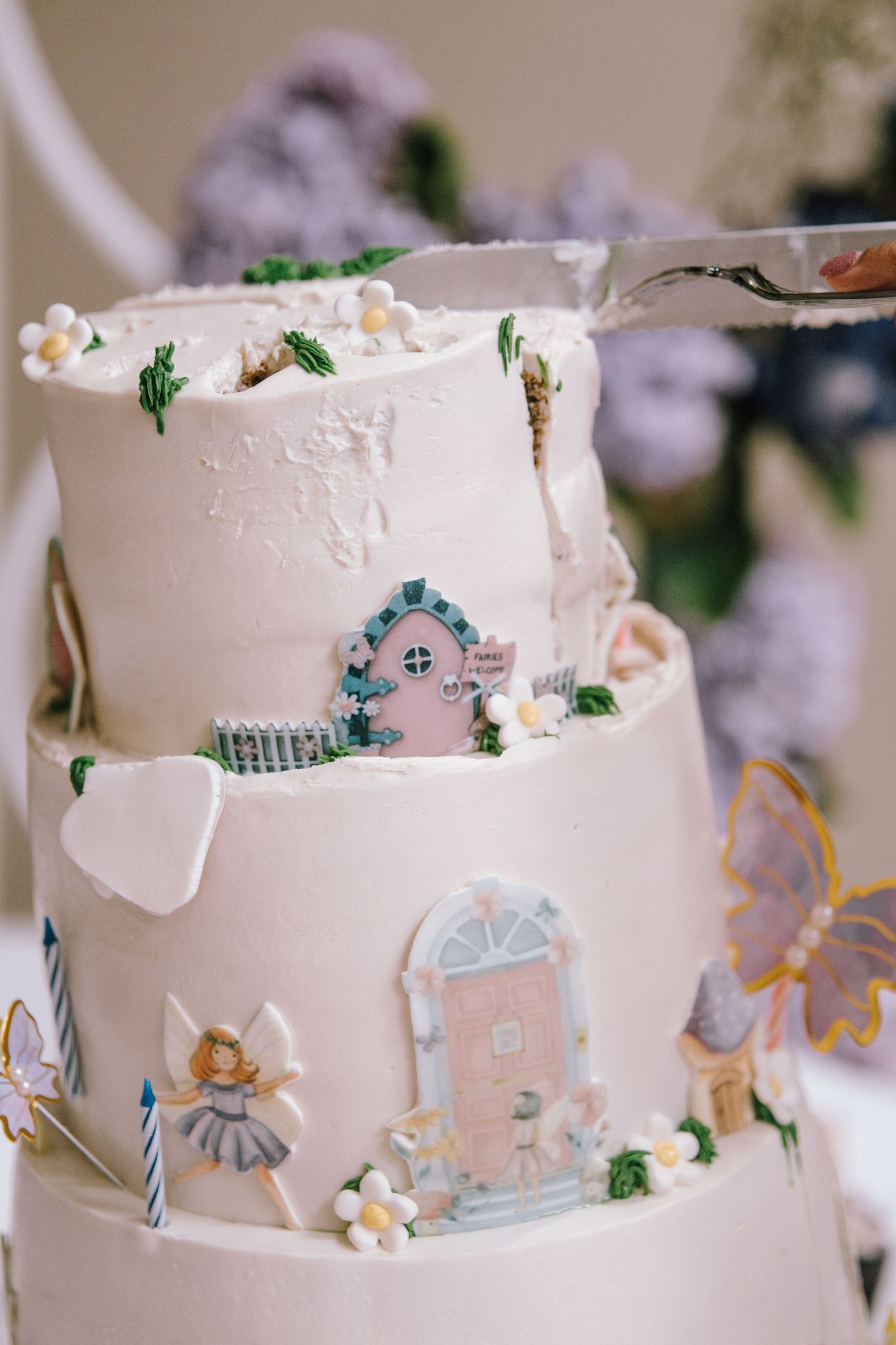 A delicate white tiered cake decorated with tiny doors, flowers and whimsical fairy-tale designs.