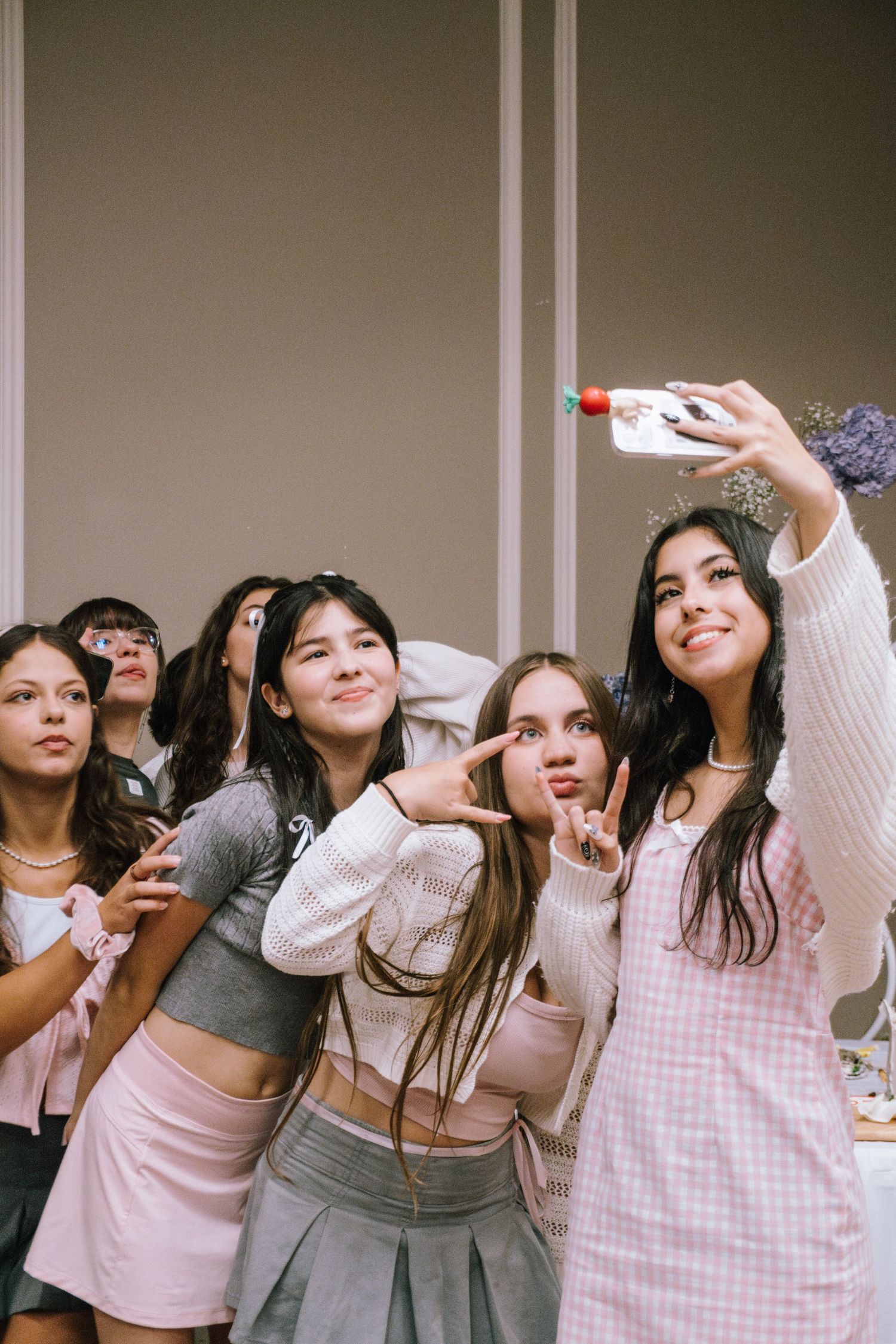 Friends taking a fun selfie together at a party wearing casual pink and gray outfits.