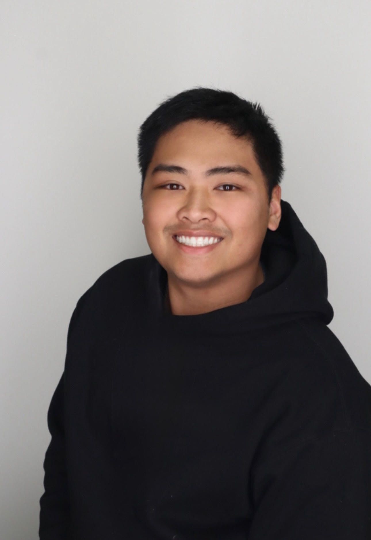Portrait against grey background wearing black hoodie.
