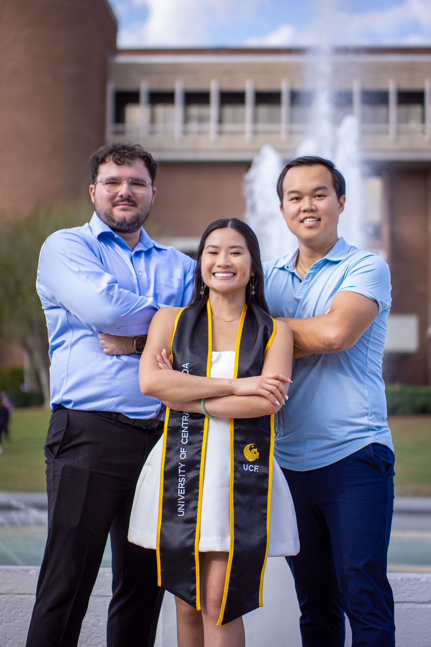 Three graduates posing together for a portrait in front of campus fountain.