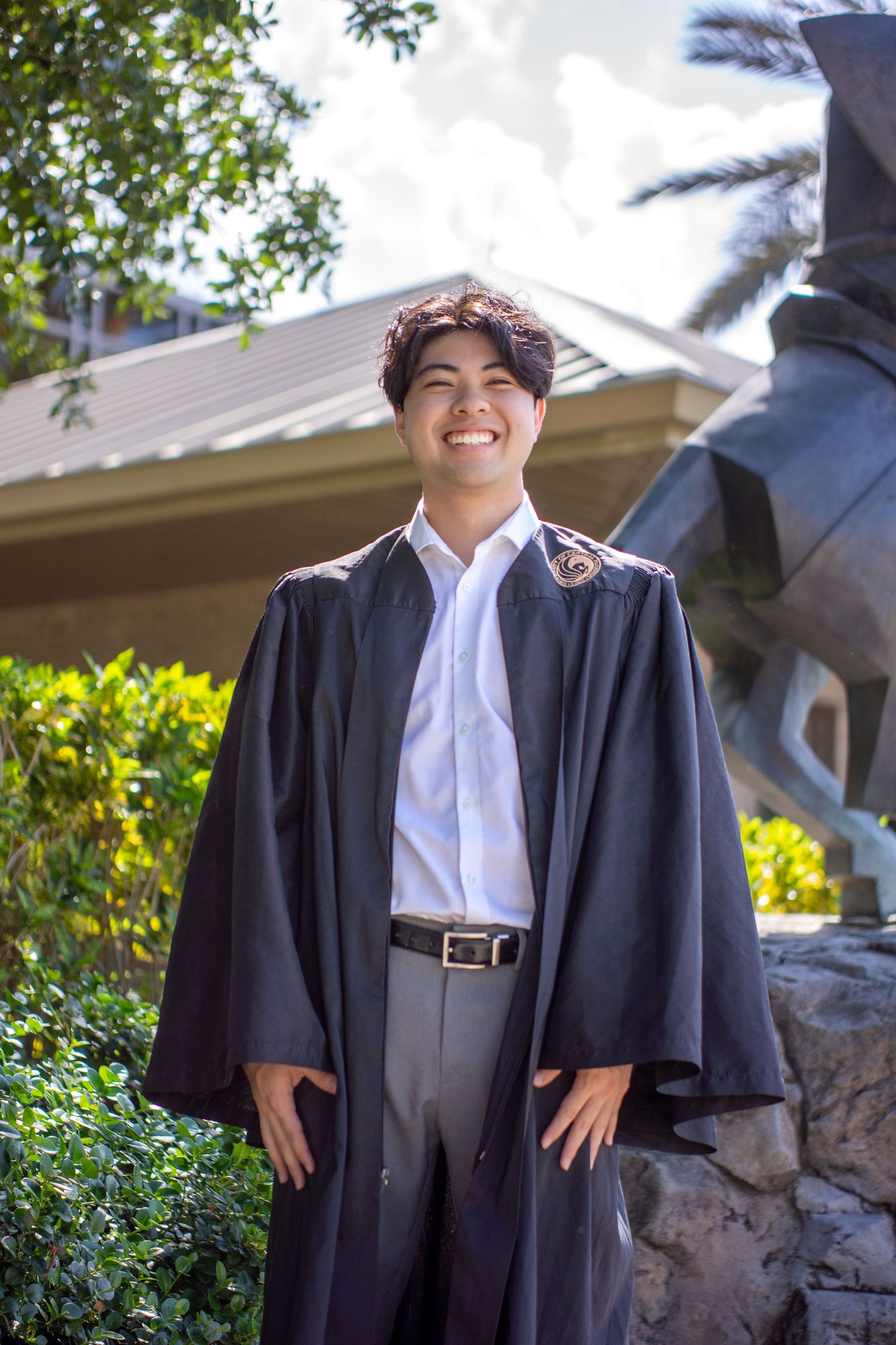Graduate in traditional academic regalia poses by landscaping.