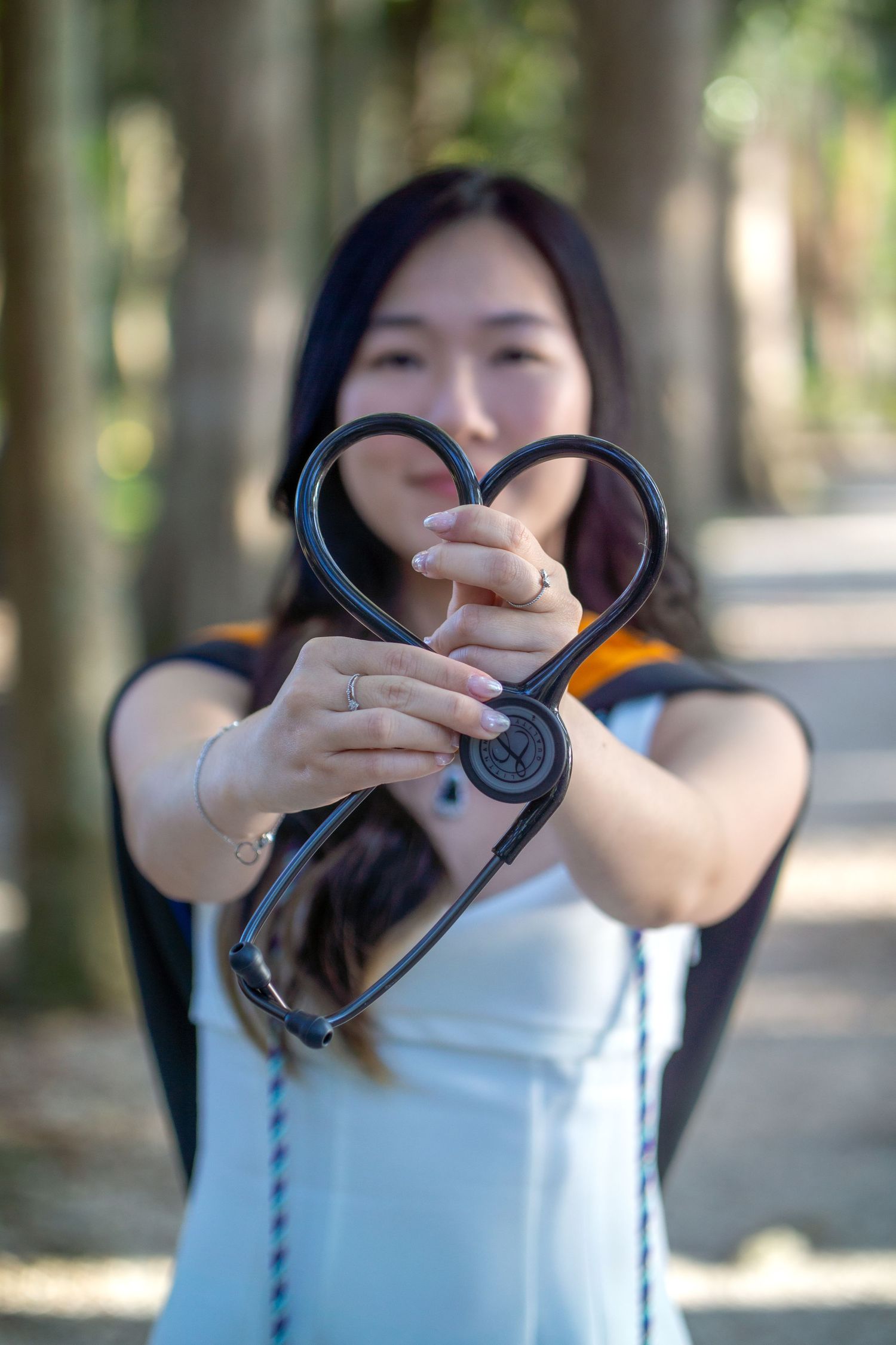 Graduate holding up stethoscope in heart shape outdoors.