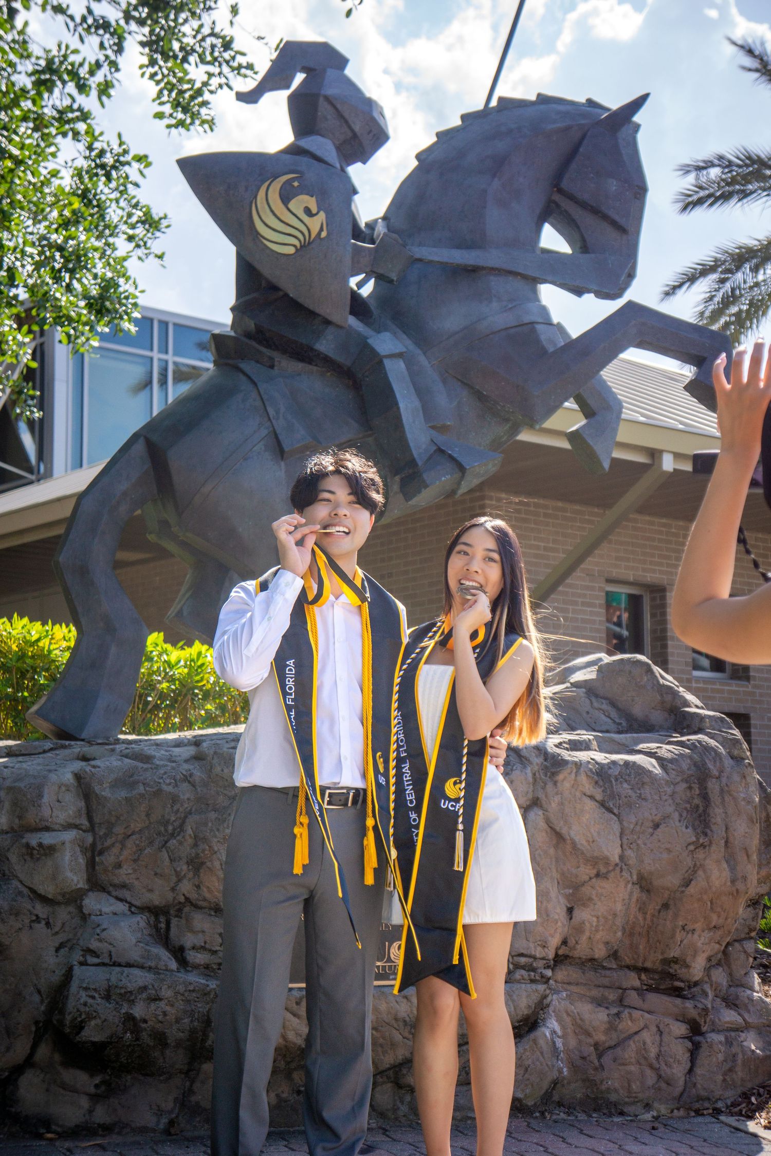 Graduates pose by UCF Knightro statue in graduation attire.