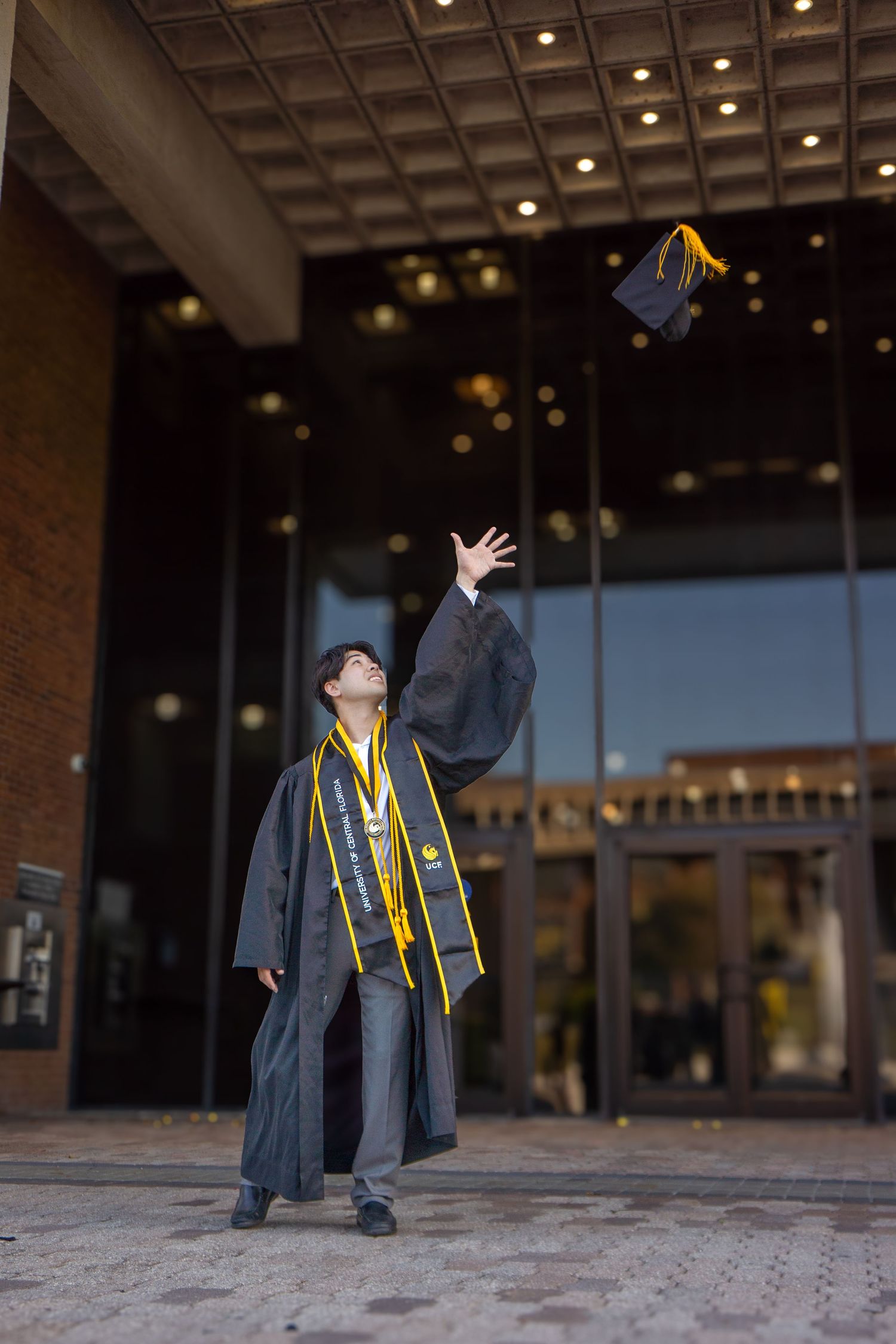 Graduate in black gown and gold sash throwing cap in the air.
