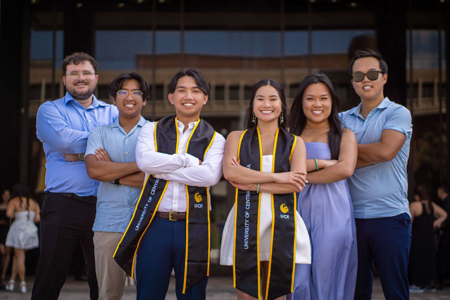 Group of graduates in formal attire and stoles pose together.