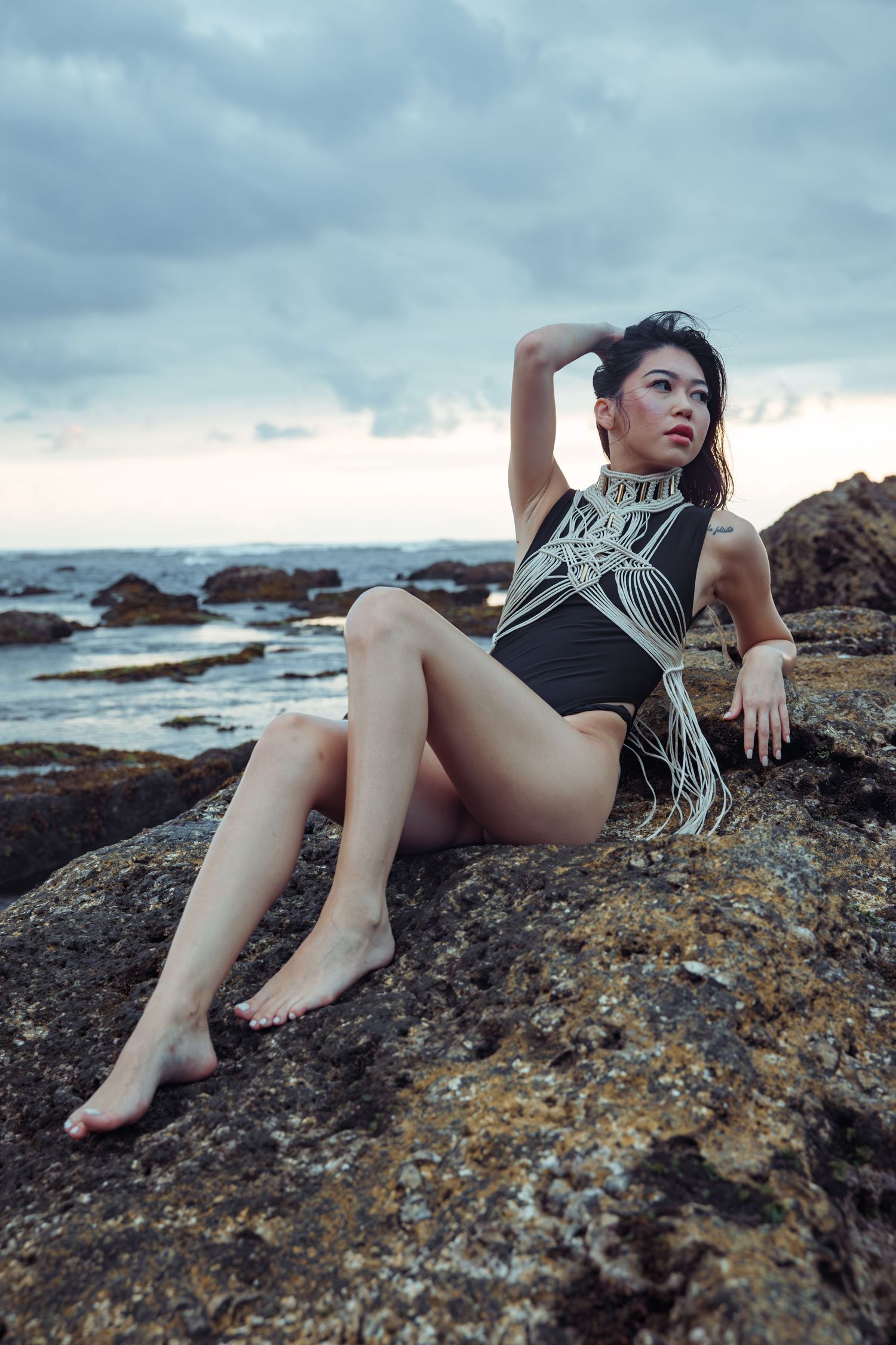 A figure in black athletic wear poses dramatically on rocky coastal cliffs at sunset.
