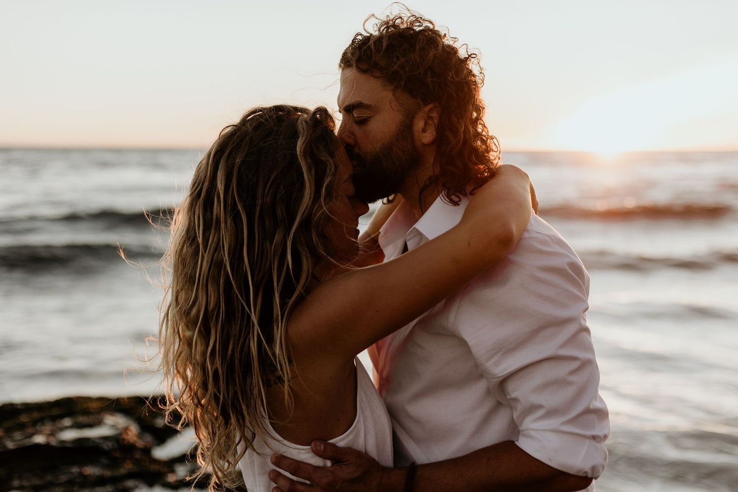 A romantic beach photoshoot at sunset with crashing waves in the background.