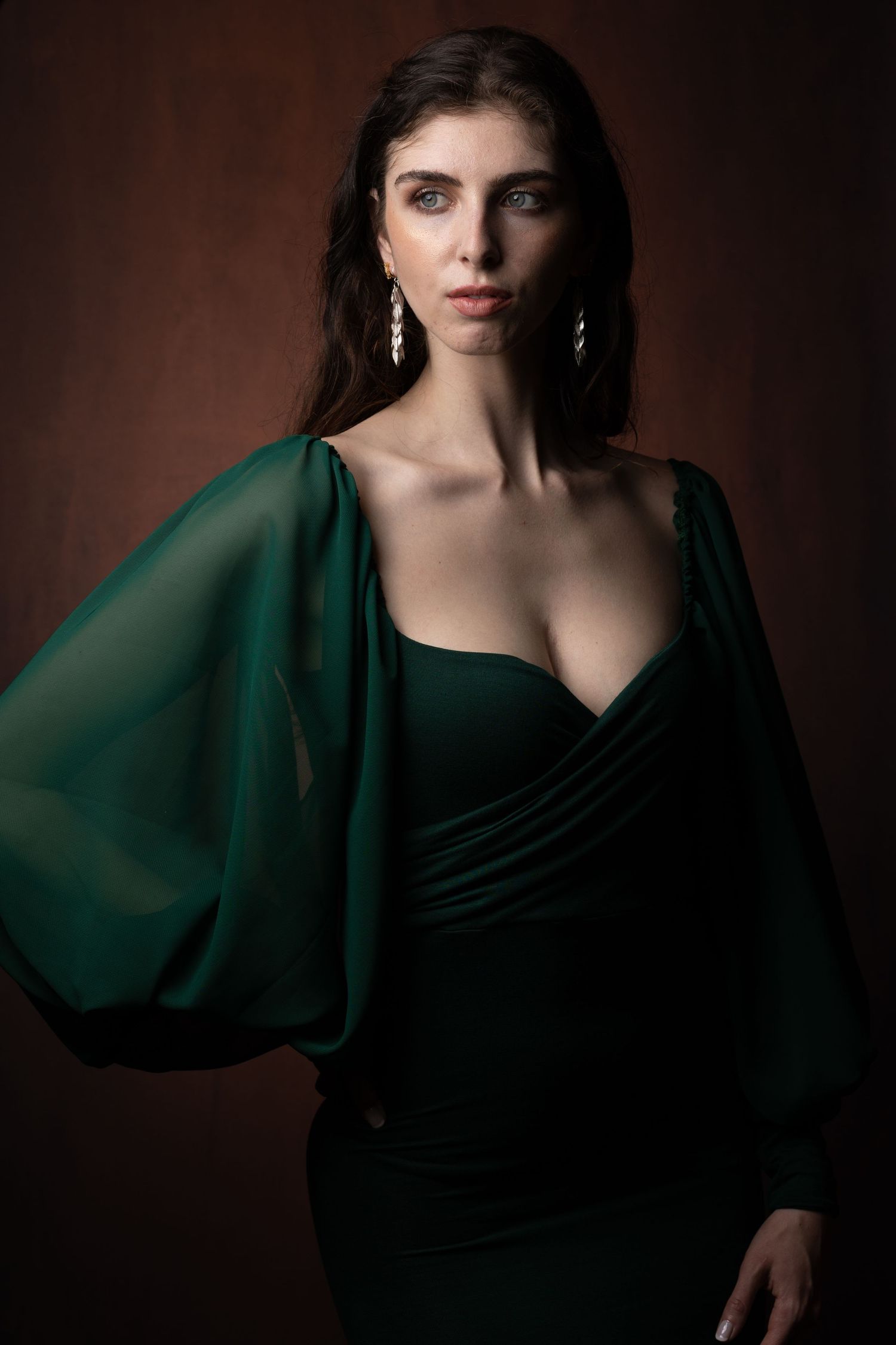 Elegant portrait in emerald green dress with dramatic sleeve detail against dark background.
