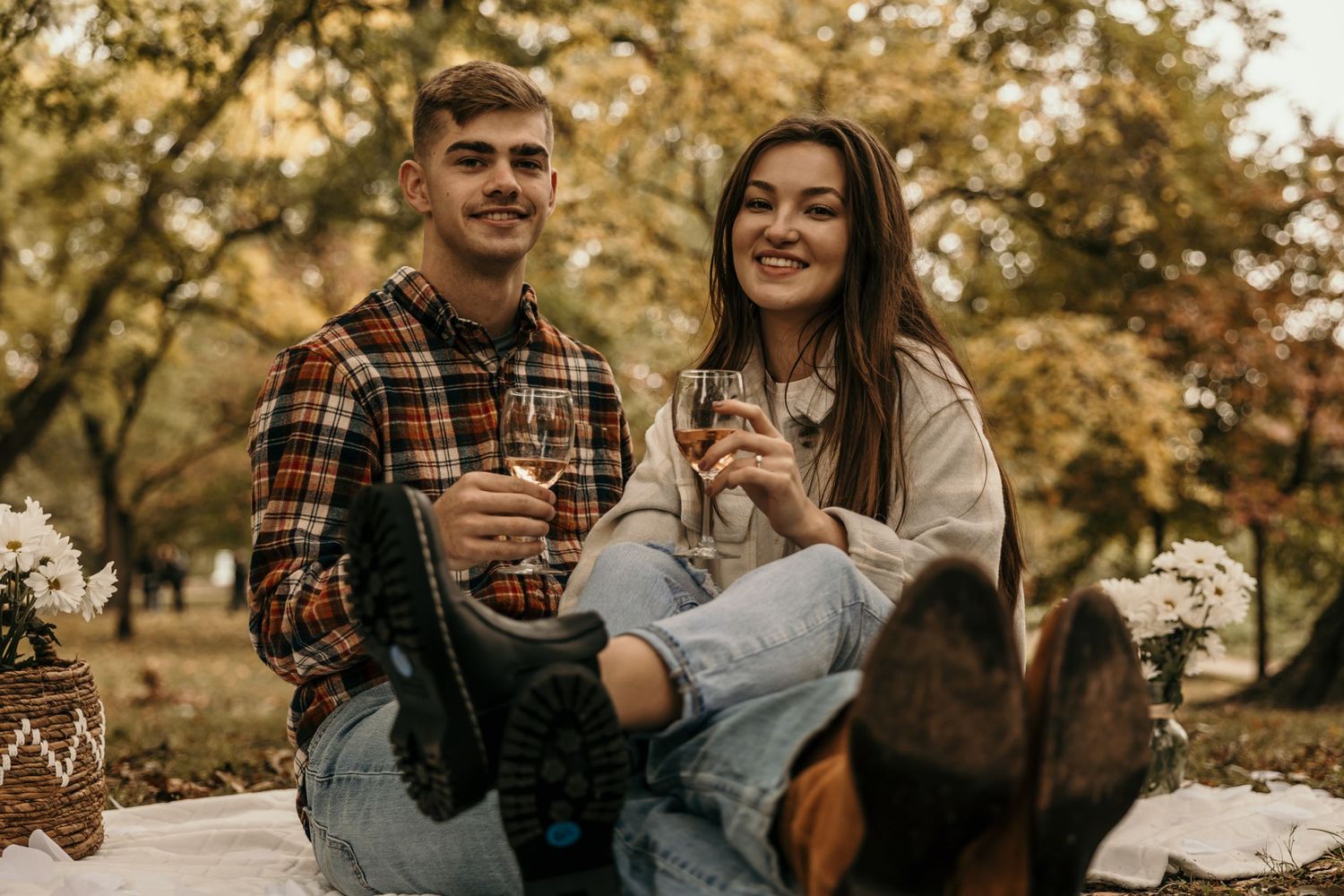 Couple enjoying wine outdoors on a picnic blanket during autumn with dog in foreground.