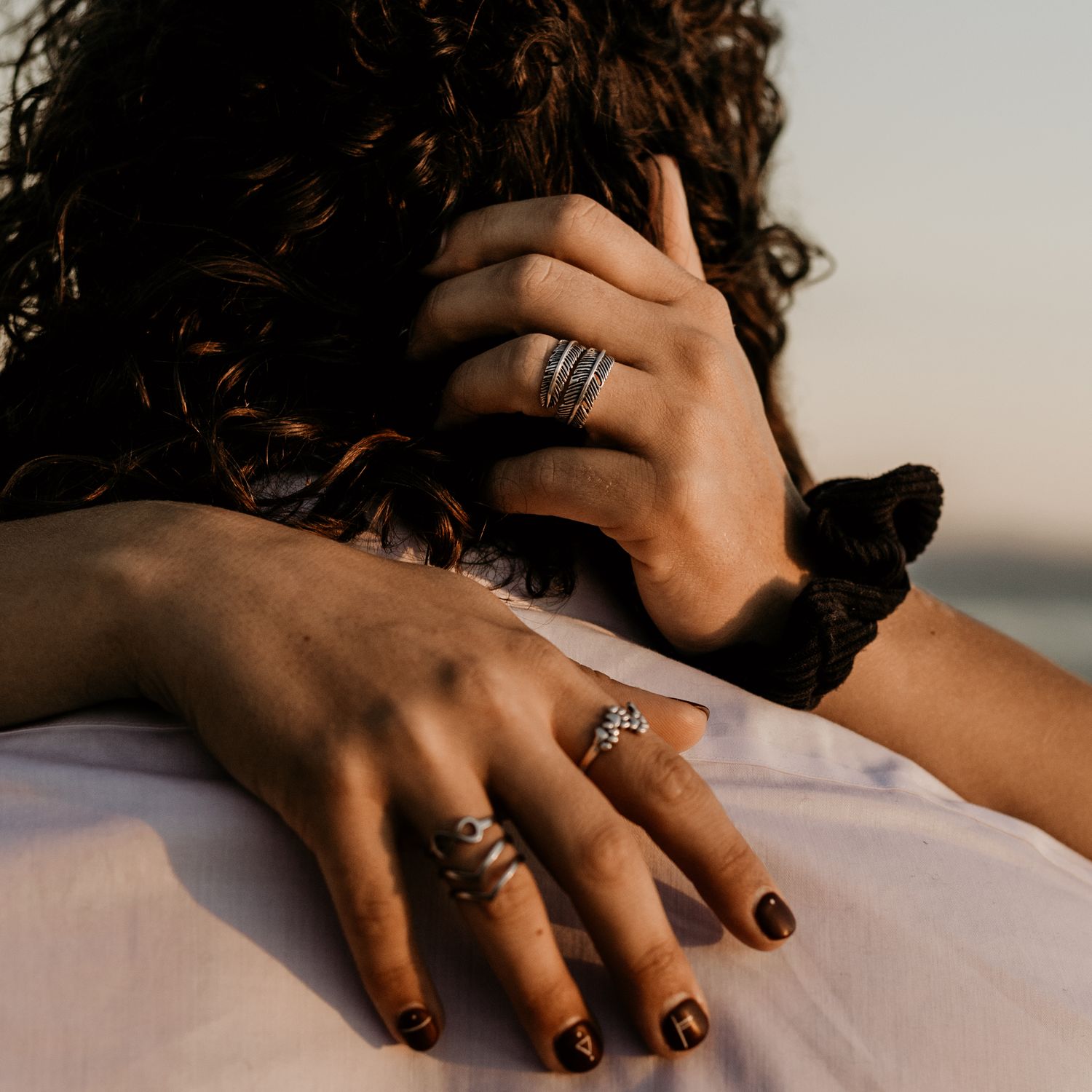 Close-up of hands with multiple rings against a soft textile background at sunset.