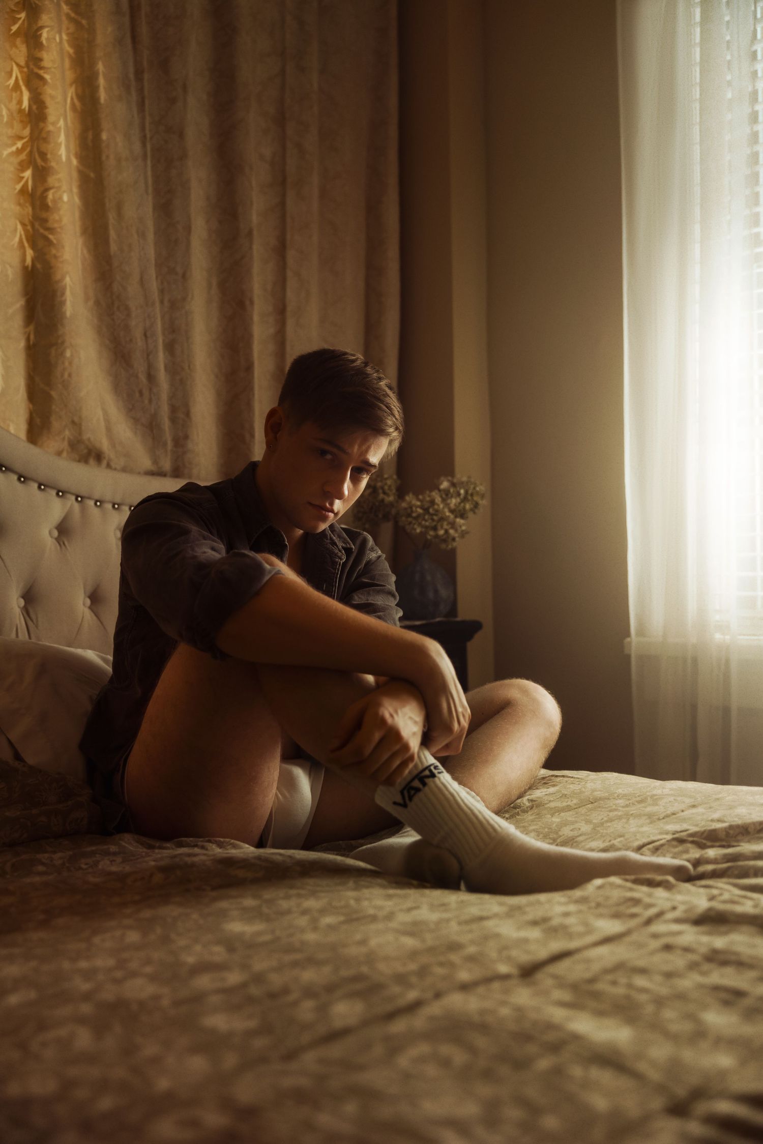 Person sitting on bed in dark moody lighting with natural sunlight coming through window.