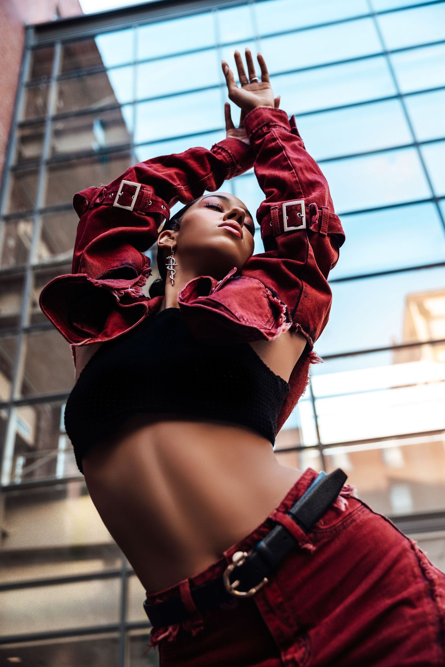 Fashion shot of person in red jacket and black crop top posing against urban building.
