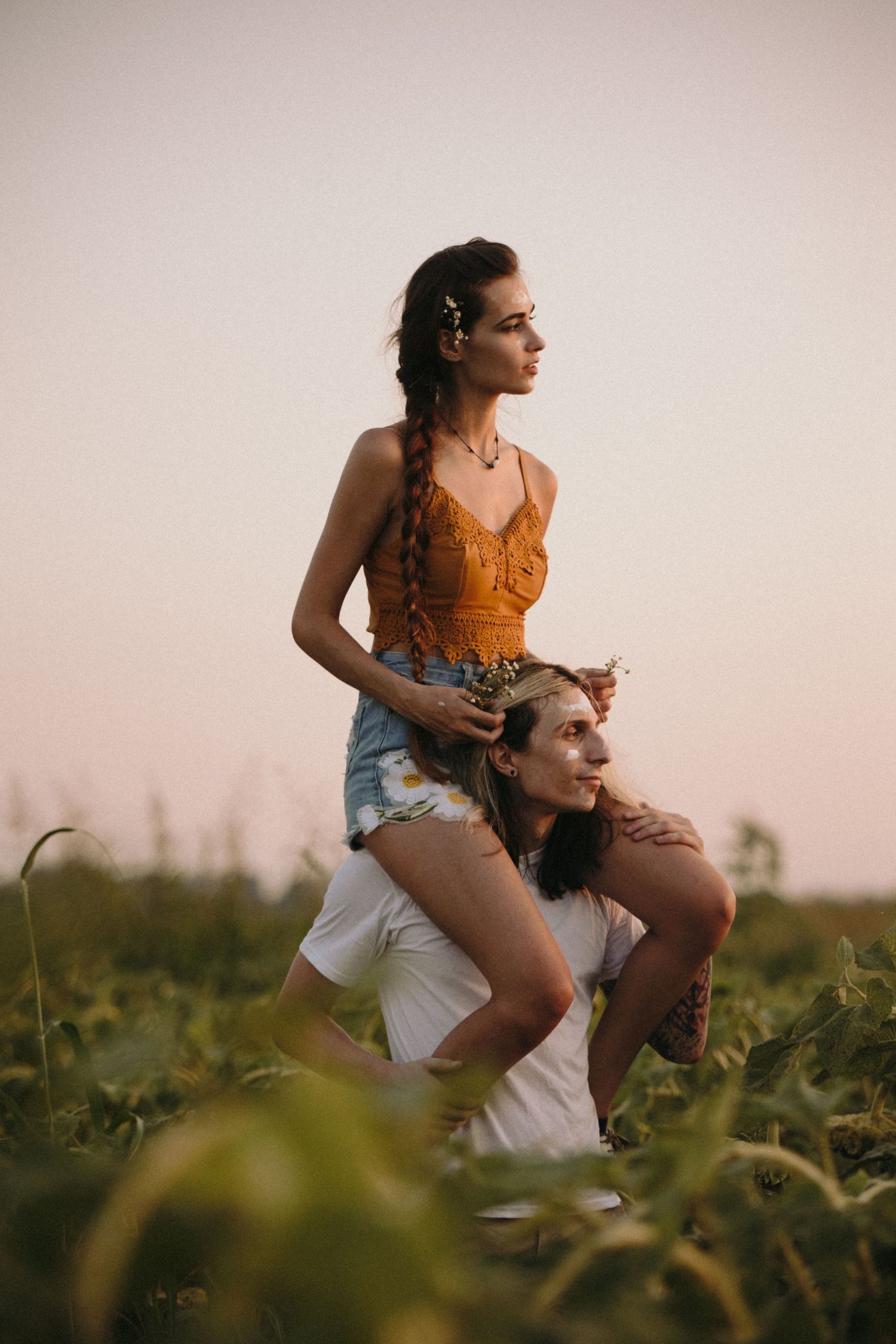 Couple enjoying a playful moment in a field at sunset as she rides on shoulders wearing an orange tank top.