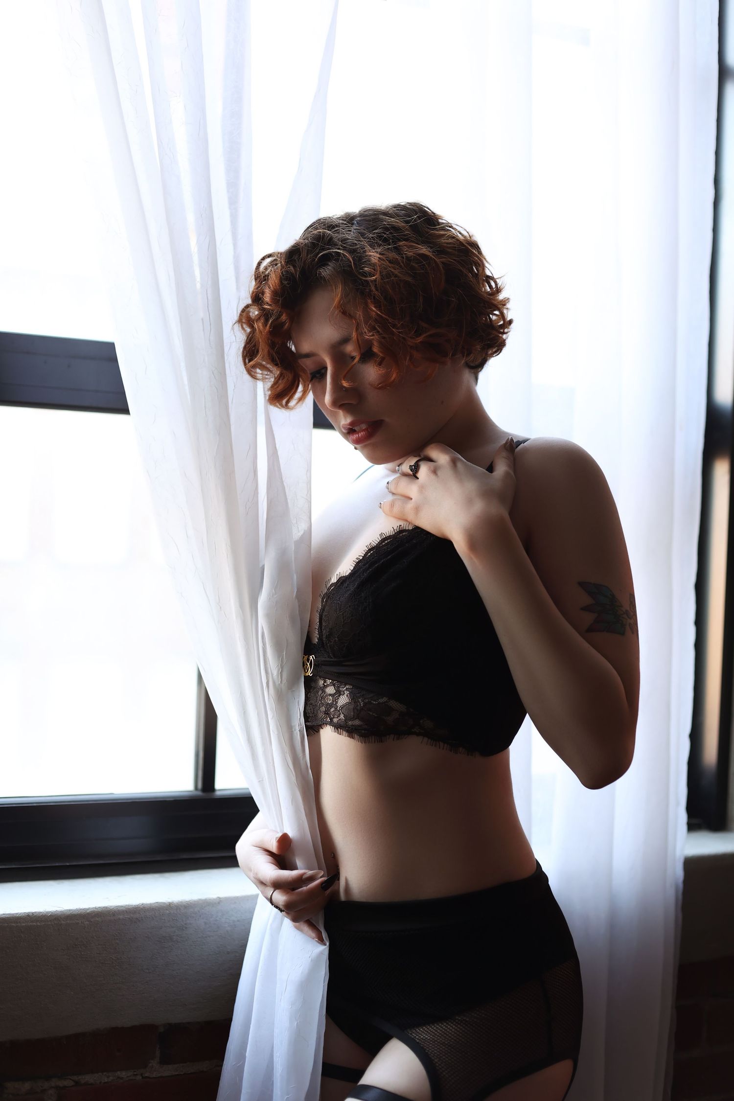 Artistic boudoir photo with white curtains and natural window lighting.