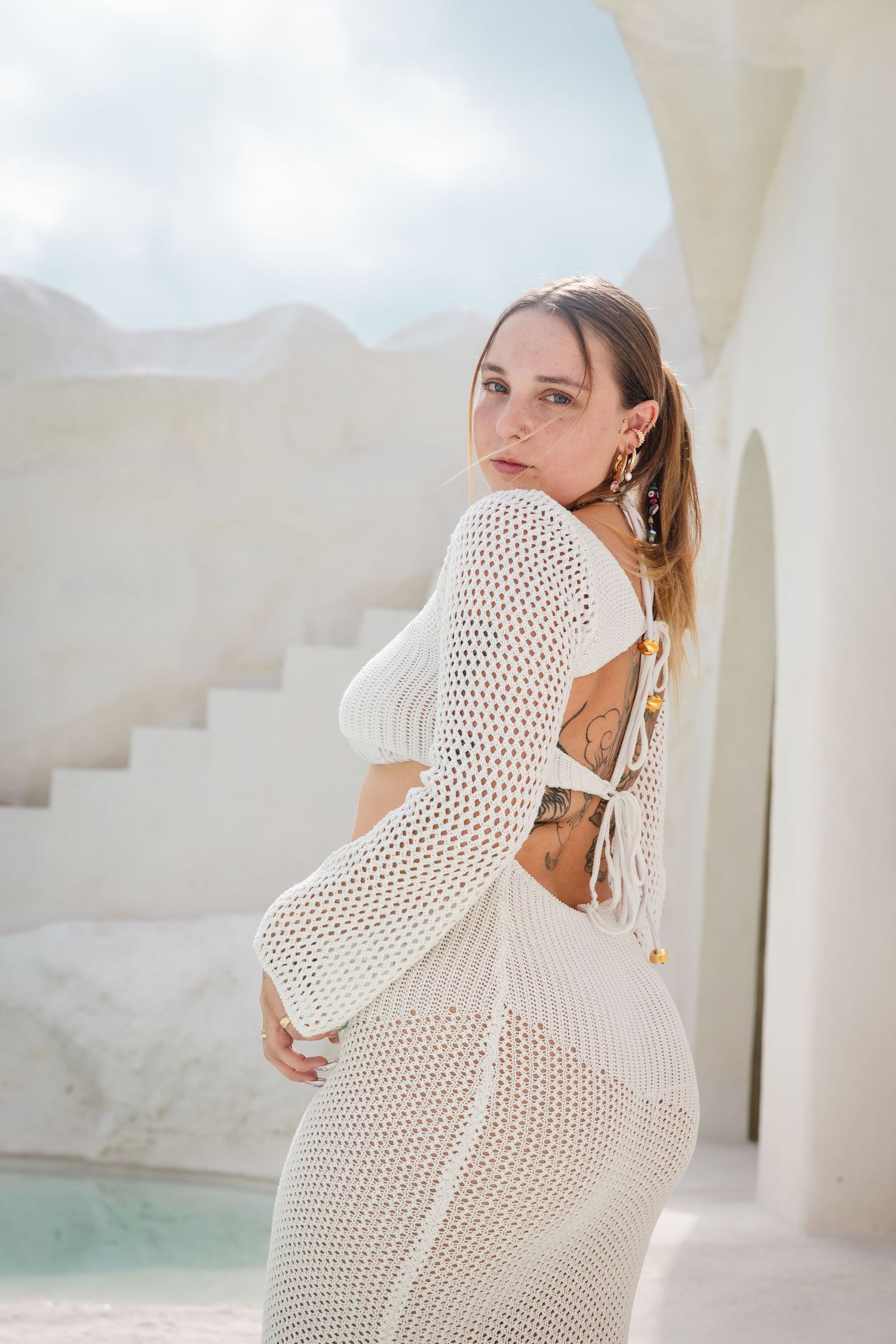 White crochet dress with open back detail and long sleeves photographed against bright white Mediterranean architecture.