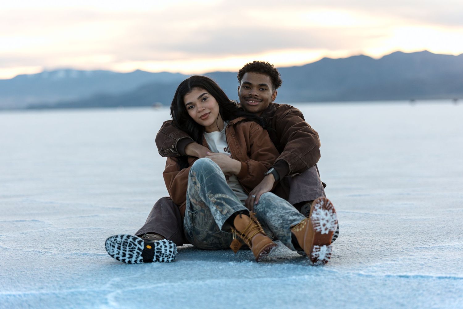 Couple sharing intimate moment on frozen landscape with mountains in distance.