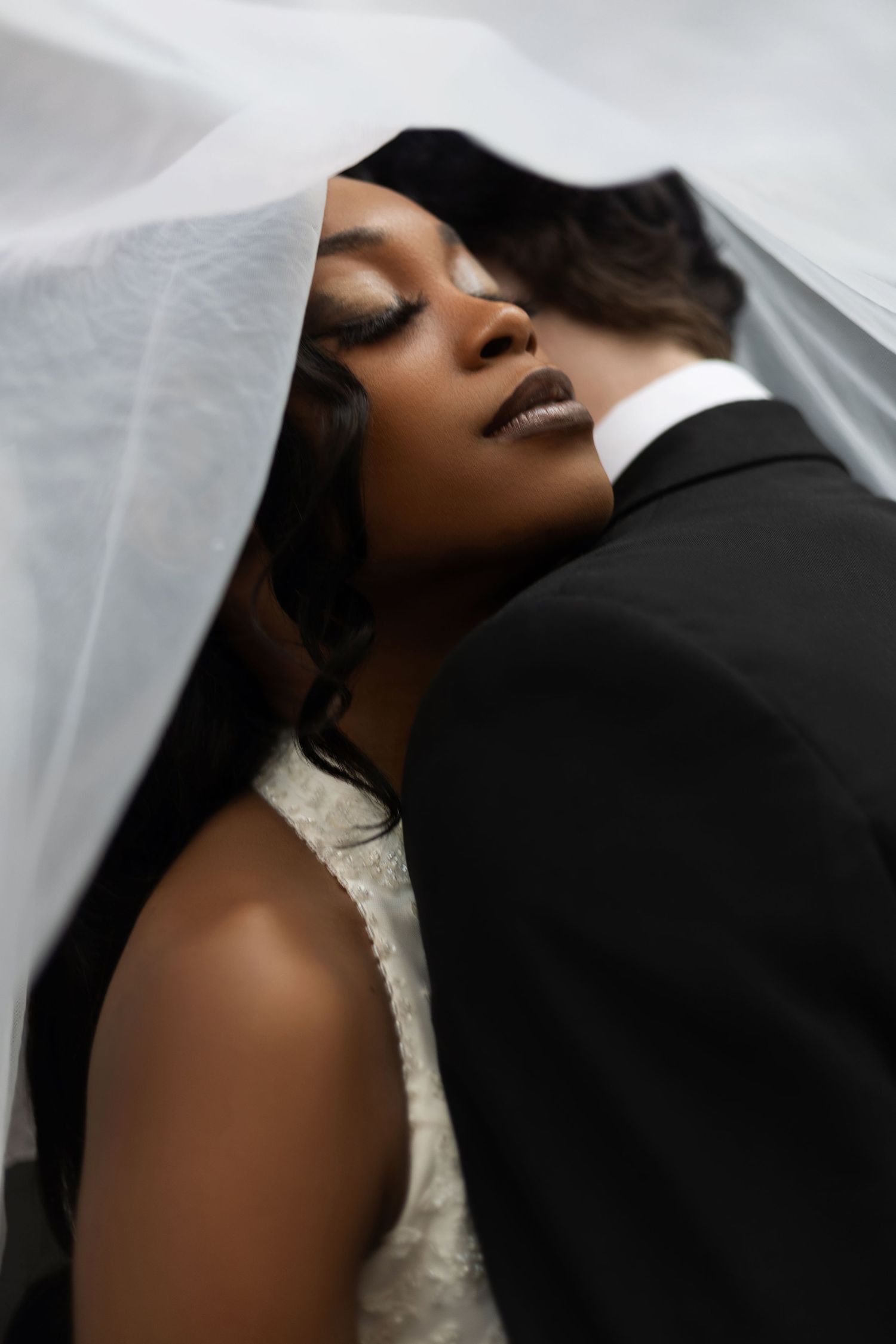 Artistic close-up wedding photograph through white veil with soft lighting.