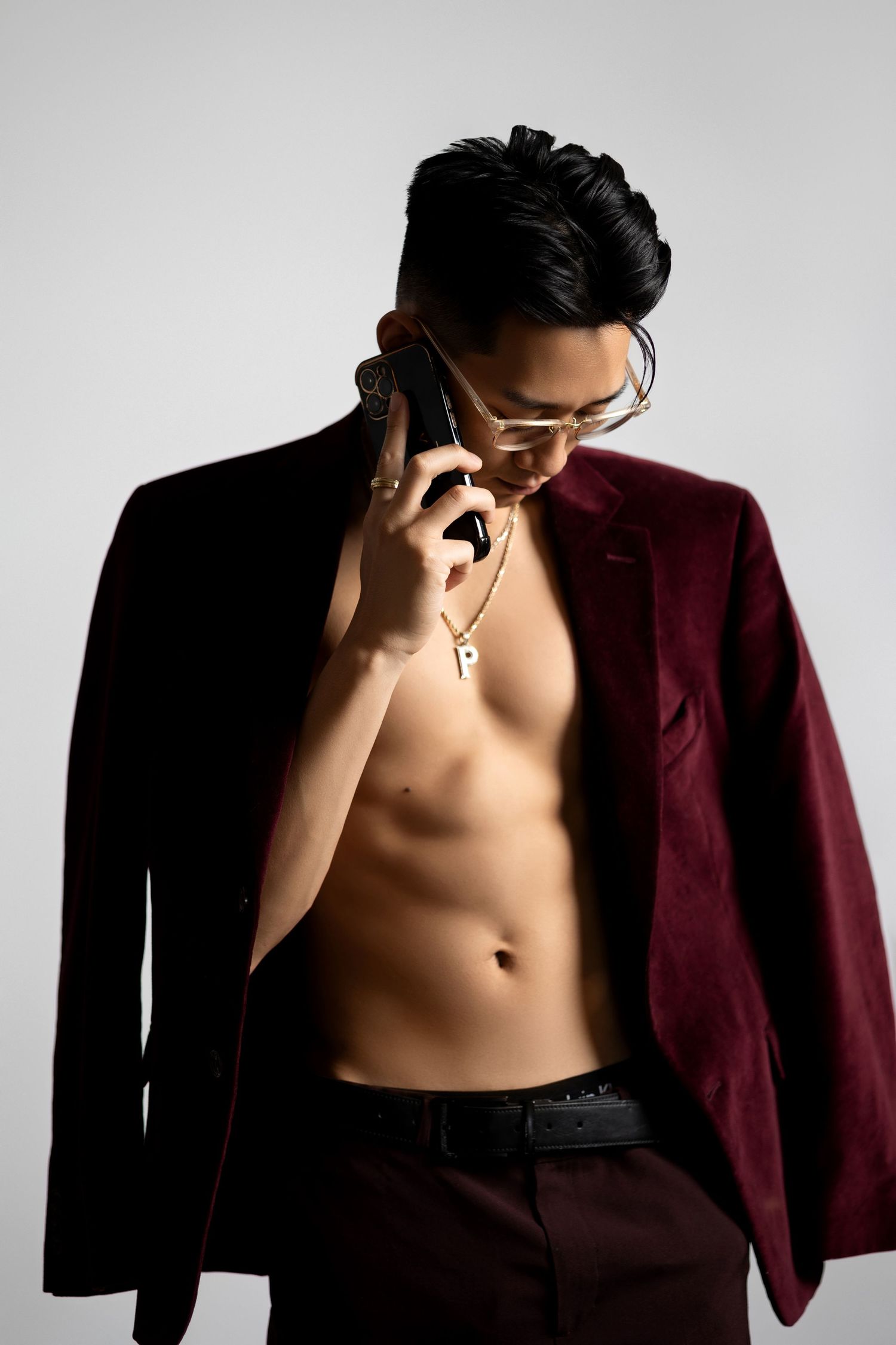 Dramatic portrait of model in burgundy blazer holding phone against light background.