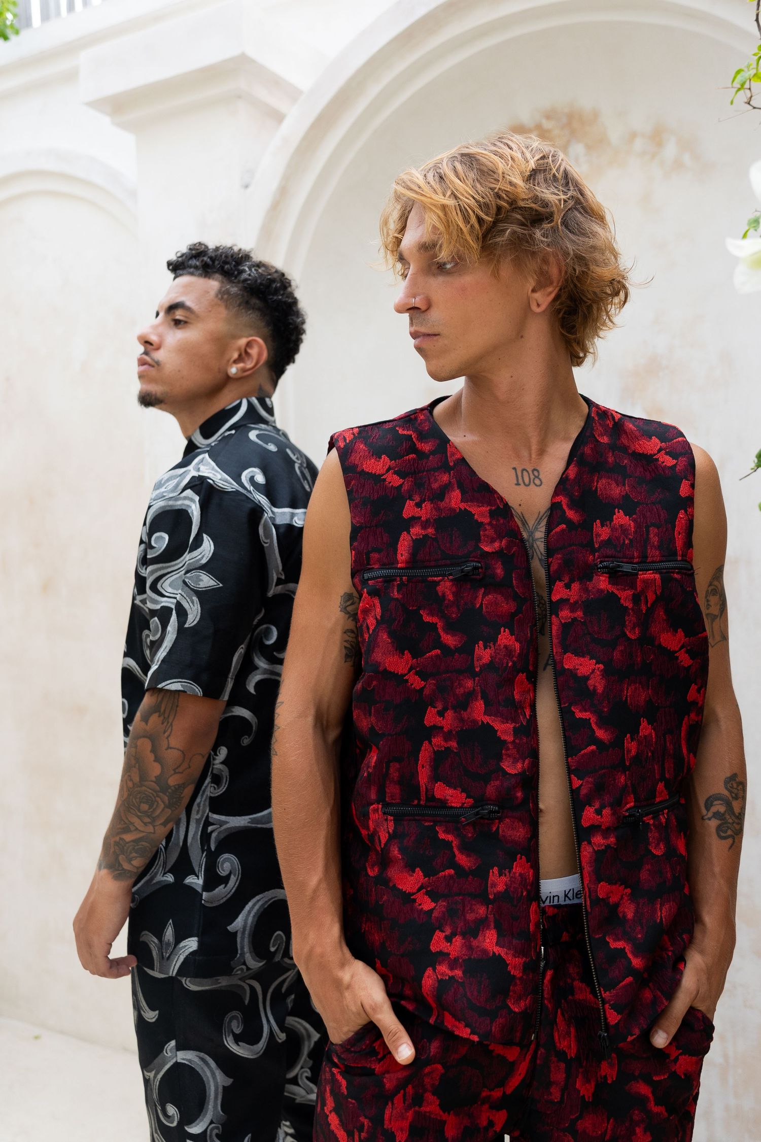 Two models wearing contrasting urban streetwear with black and gray pattern versus red and black camo designs.