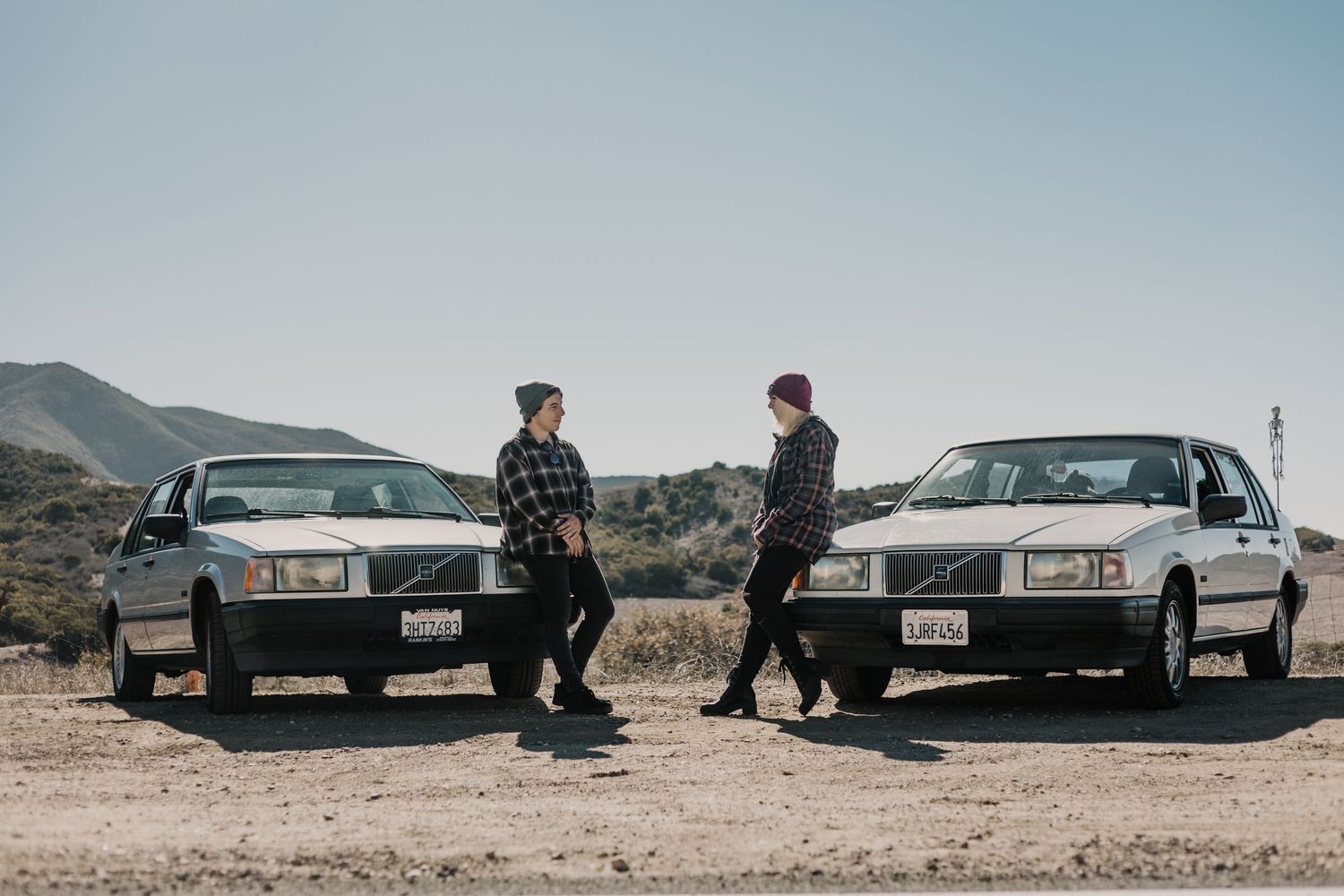 Two Volvo cars parked in a desert landscape with a couple hanging out in casual attire.