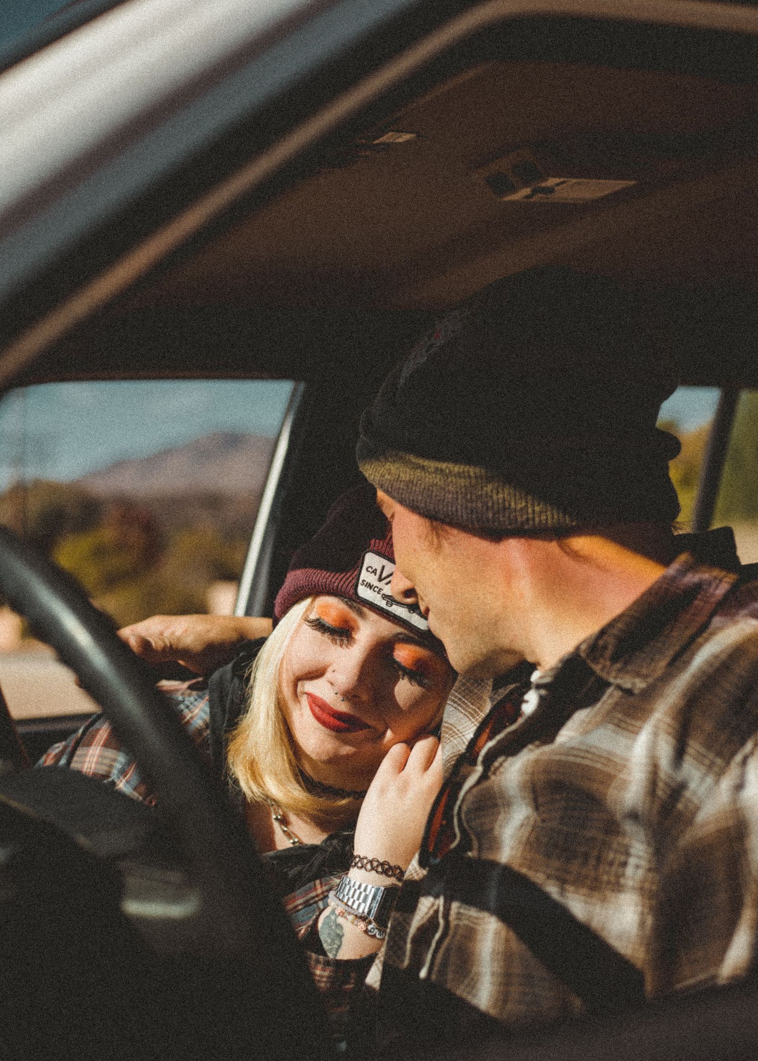 A couple sharing a tender moment inside a car with mountains visible through the window.