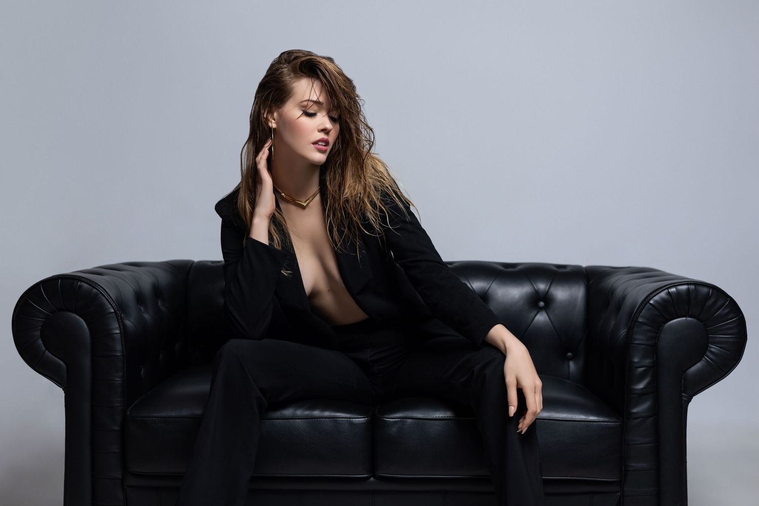 Artistic fashion shot on black leather sofa in minimalist setting.