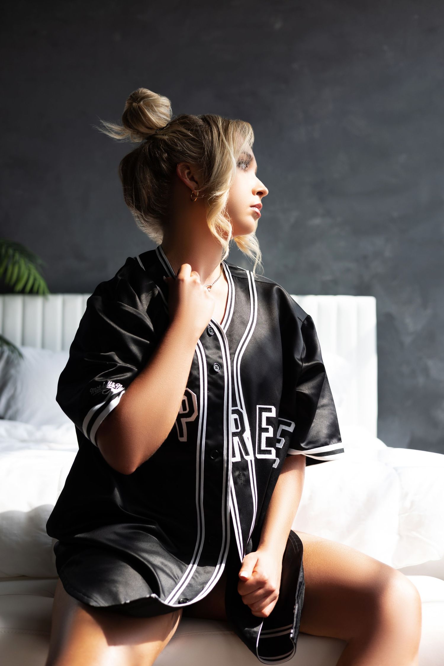 Model wearing oversized black baseball jersey in moody indoor setting.