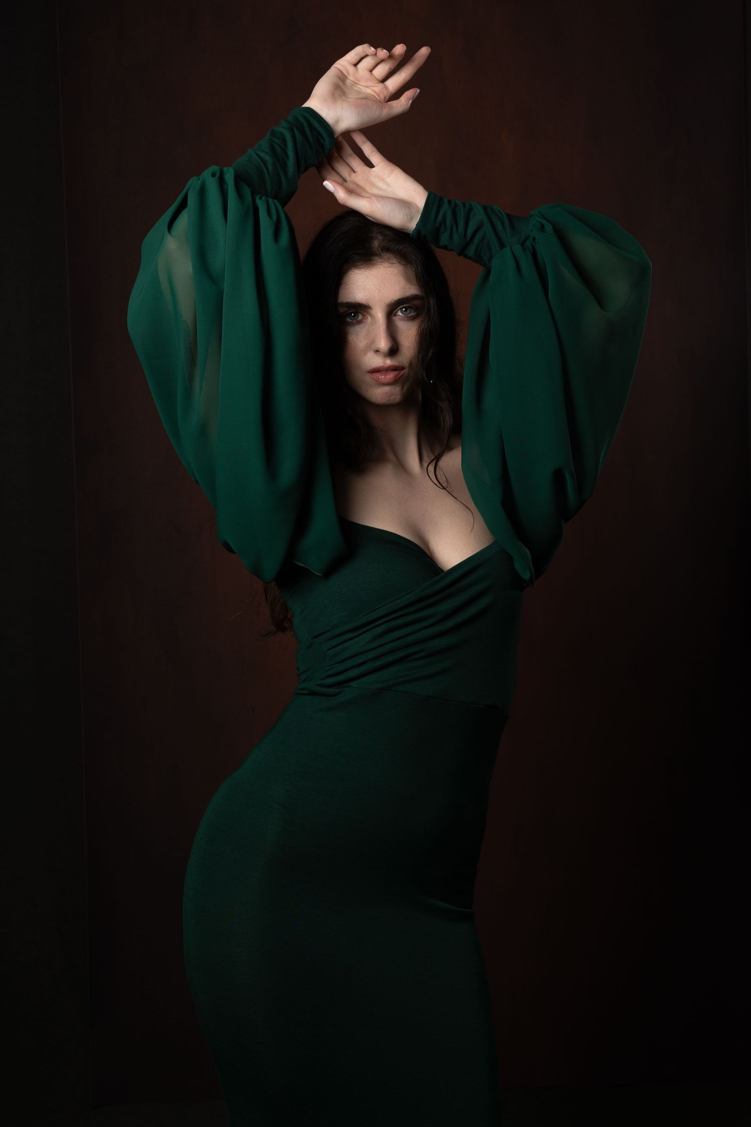 Dramatic fashion photo of model in emerald green dress with statement sleeves against dark background.