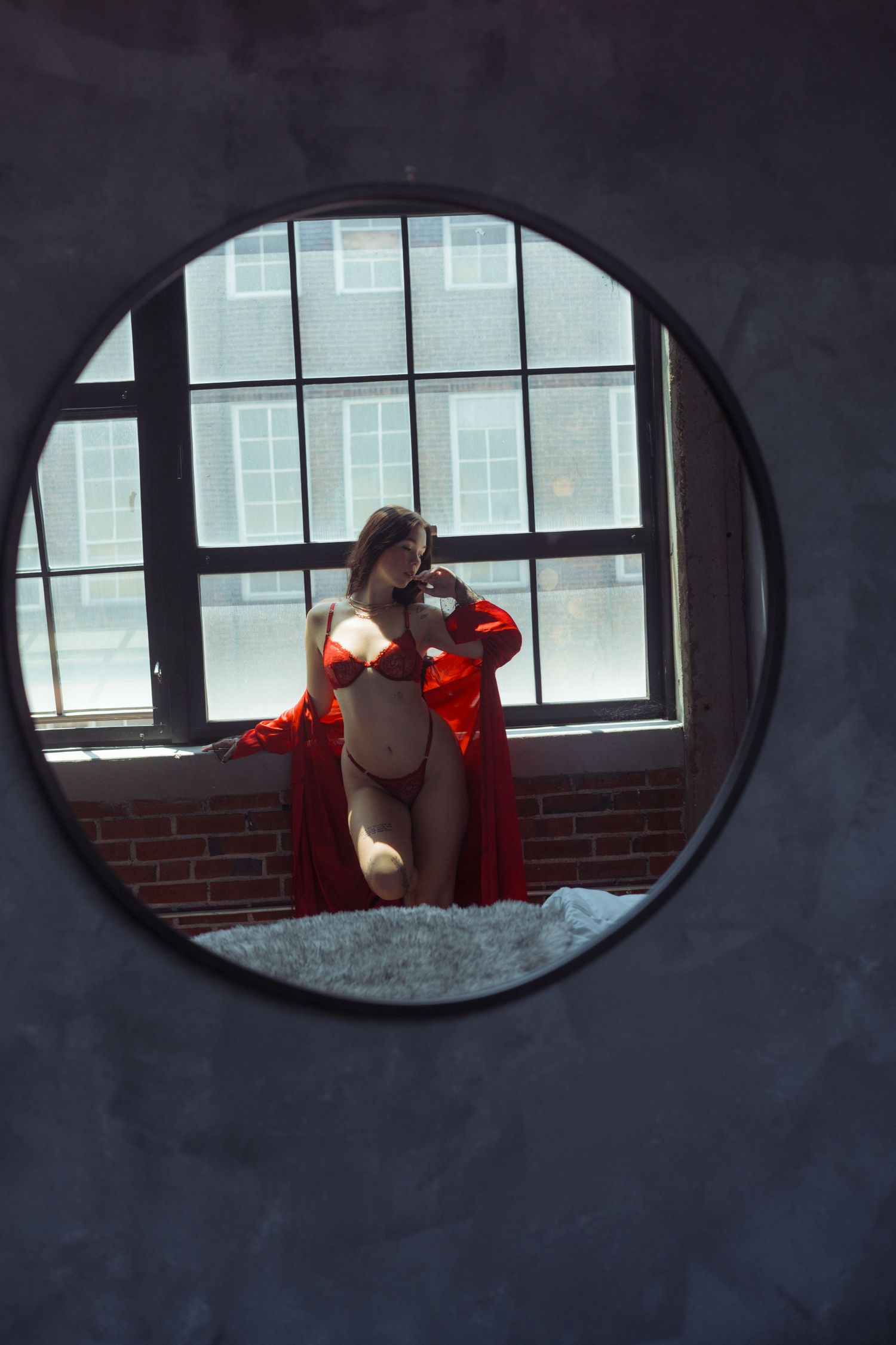 Circular mirror reflection showing figure in red robe by industrial window.