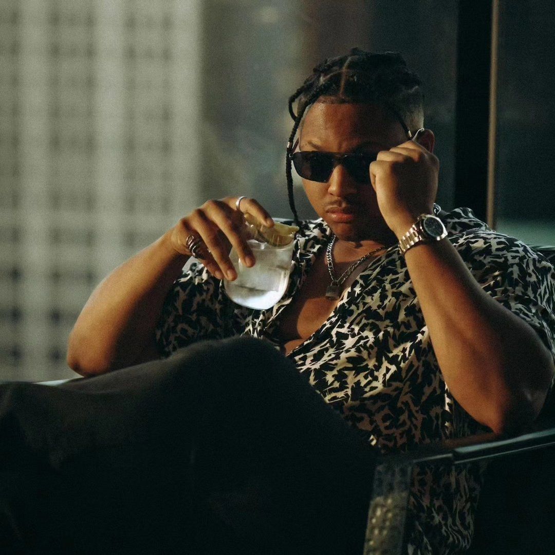 Person in animal print outfit relaxing with sunglasses and beverage.