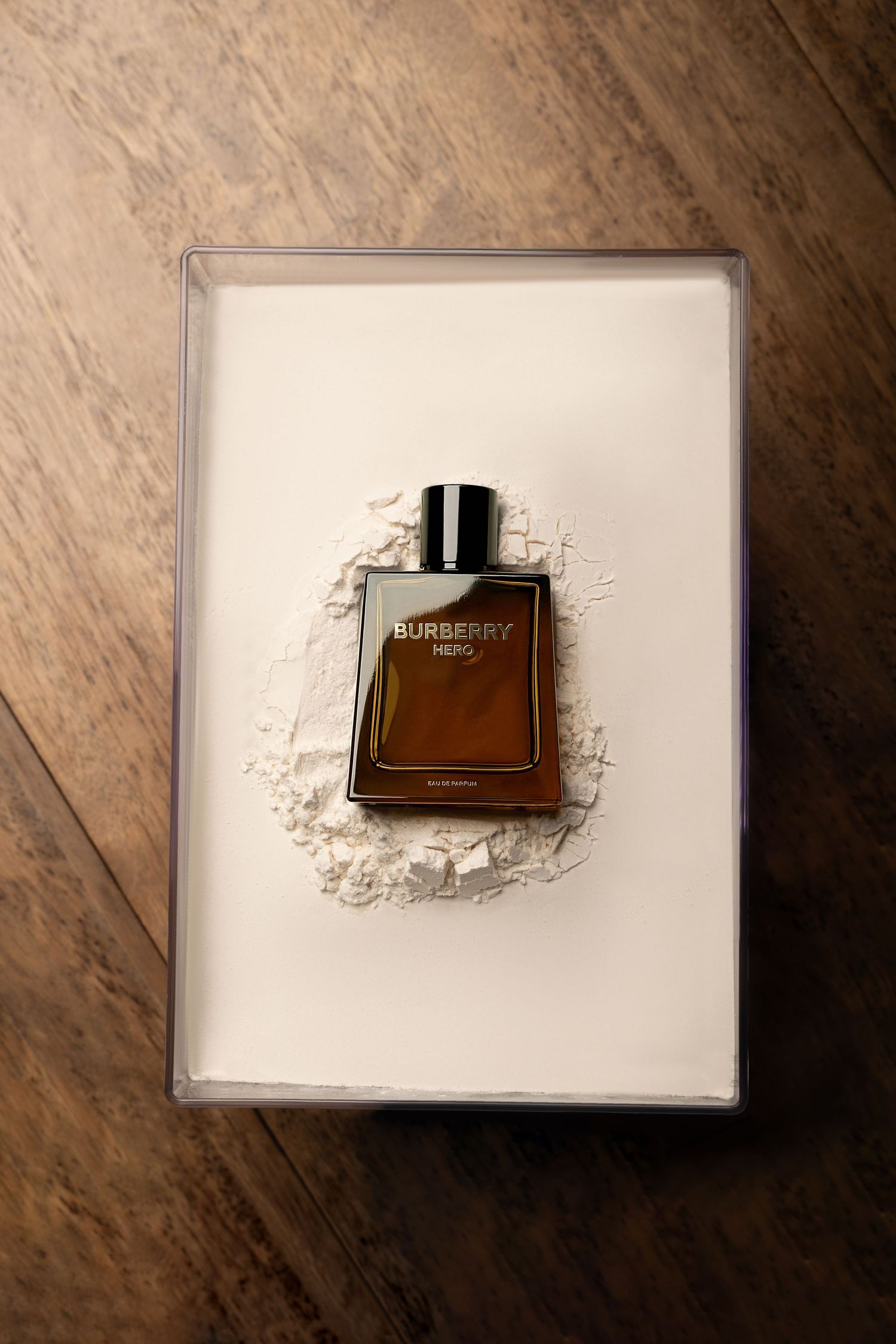 A brown perfume bottle placed on white surface with powder scattered around it, displayed in artistic composition on wooden background.