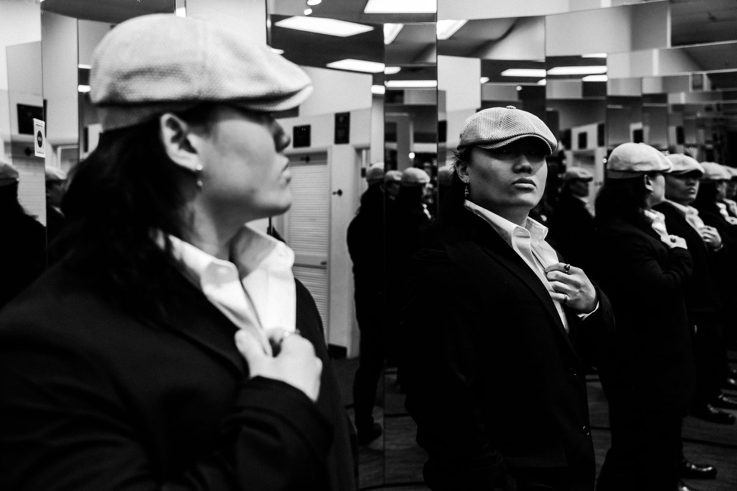 Artistic black and white photograph showing two people wearing flat caps in an indoor setting.