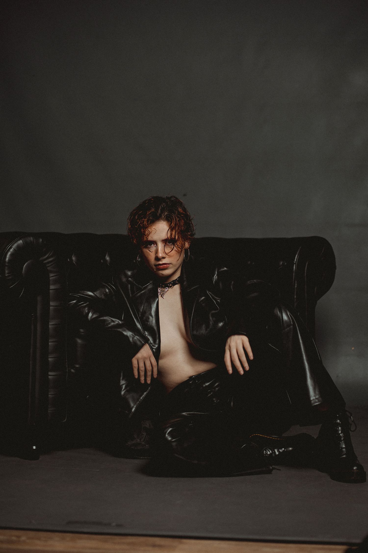 Dramatic fashion portrait on leather couch featuring dark jacket and moody lighting.
