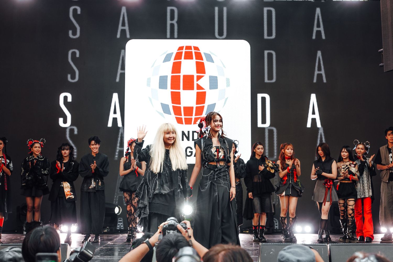 Performers on stage at a concert with SABUDA text illuminated overhead and a large audience in black attire.