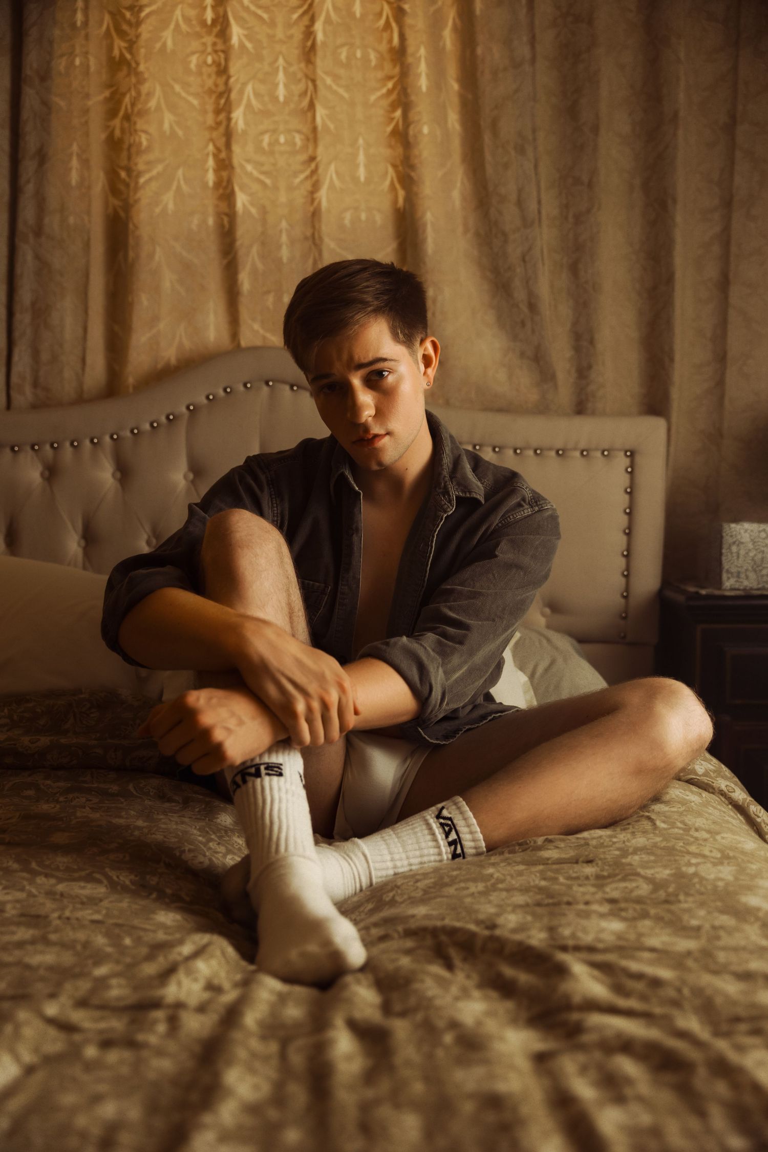 Artistic portrait of person in open shirt and socks on textured bedding.