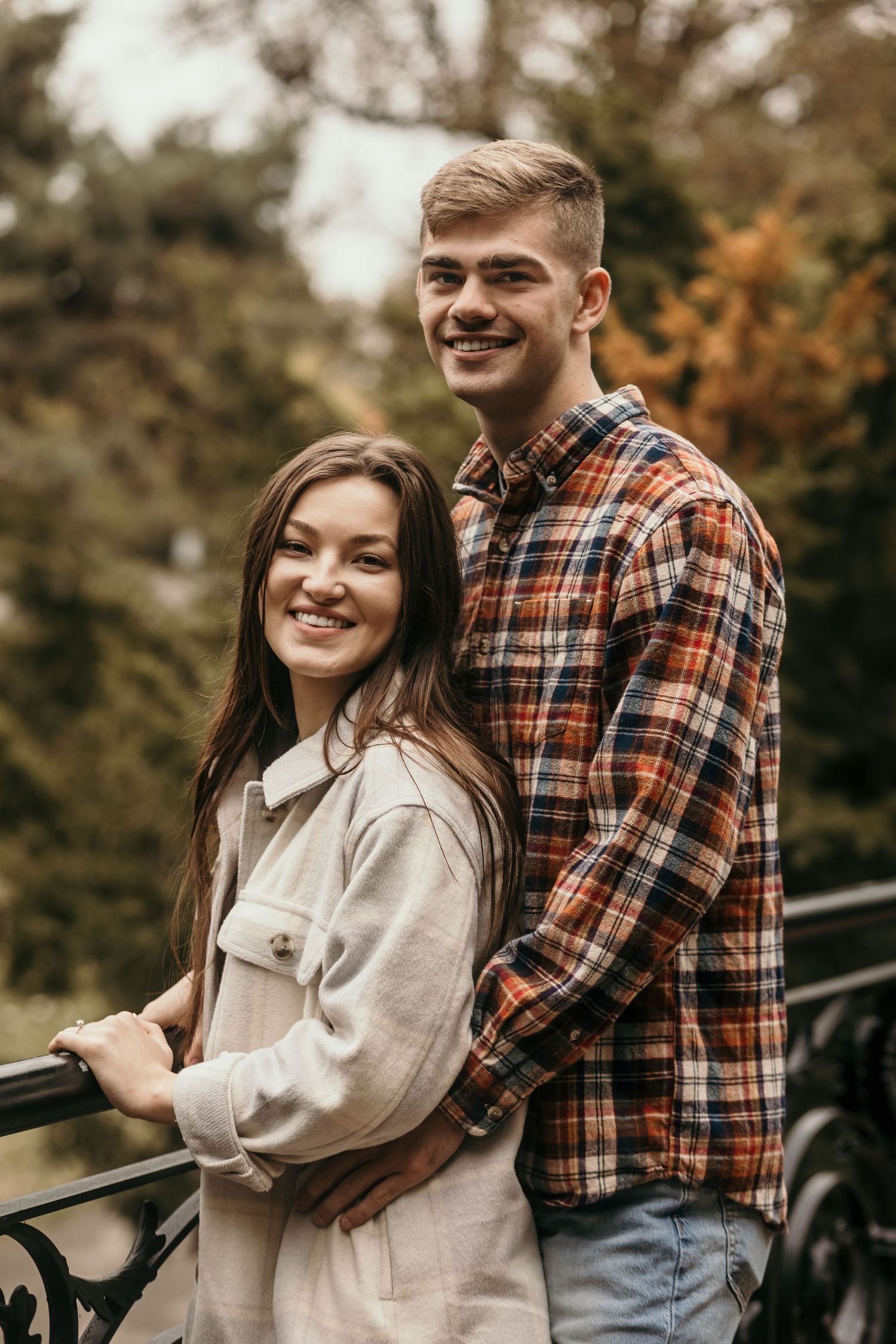 Young couple in casual fall clothing standing together on bridge during autumn outdoor photoshoot.