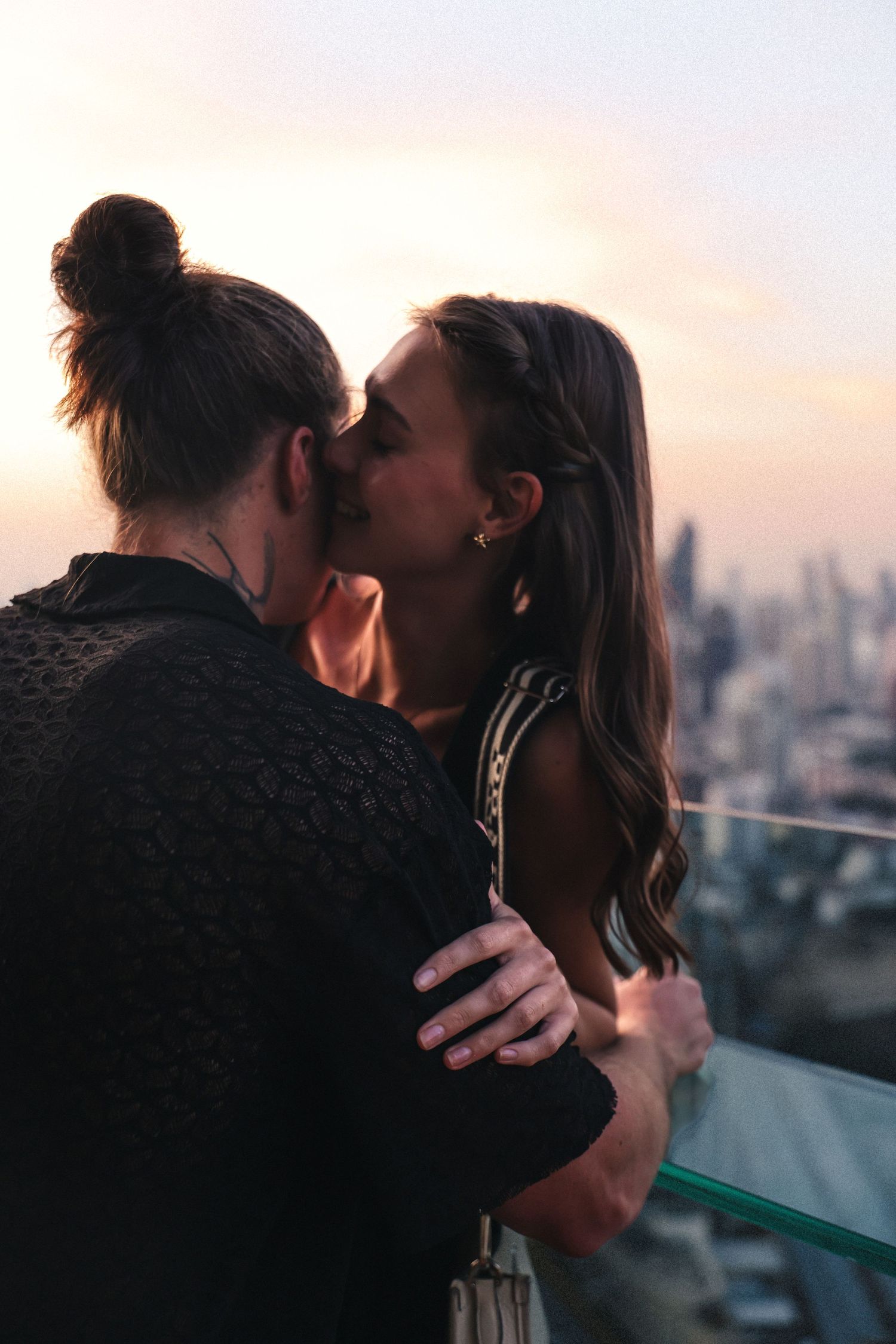 Romantic rooftop moment between couple during sunset with city skyline backdrop.