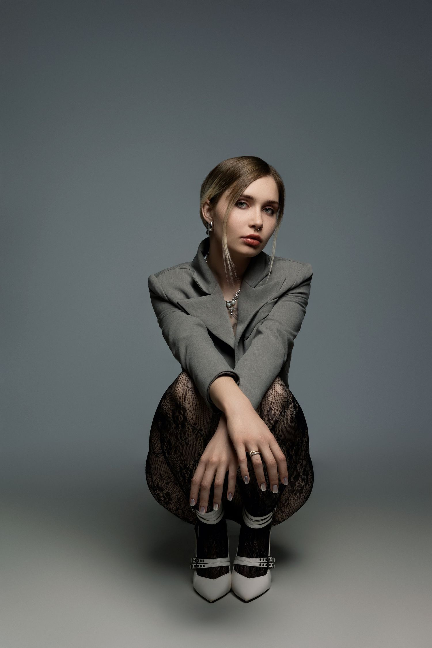 Studio portrait in gray blazer and lace skirt crouching in dramatic lighting.