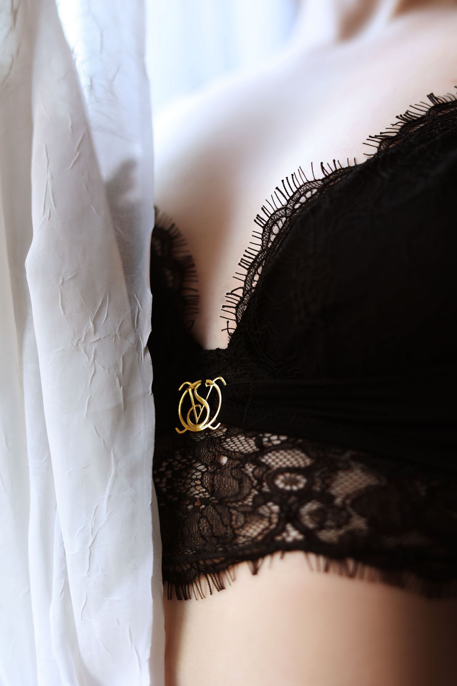 Black lace lingerie detail with gold decorative clasp against white fabric.