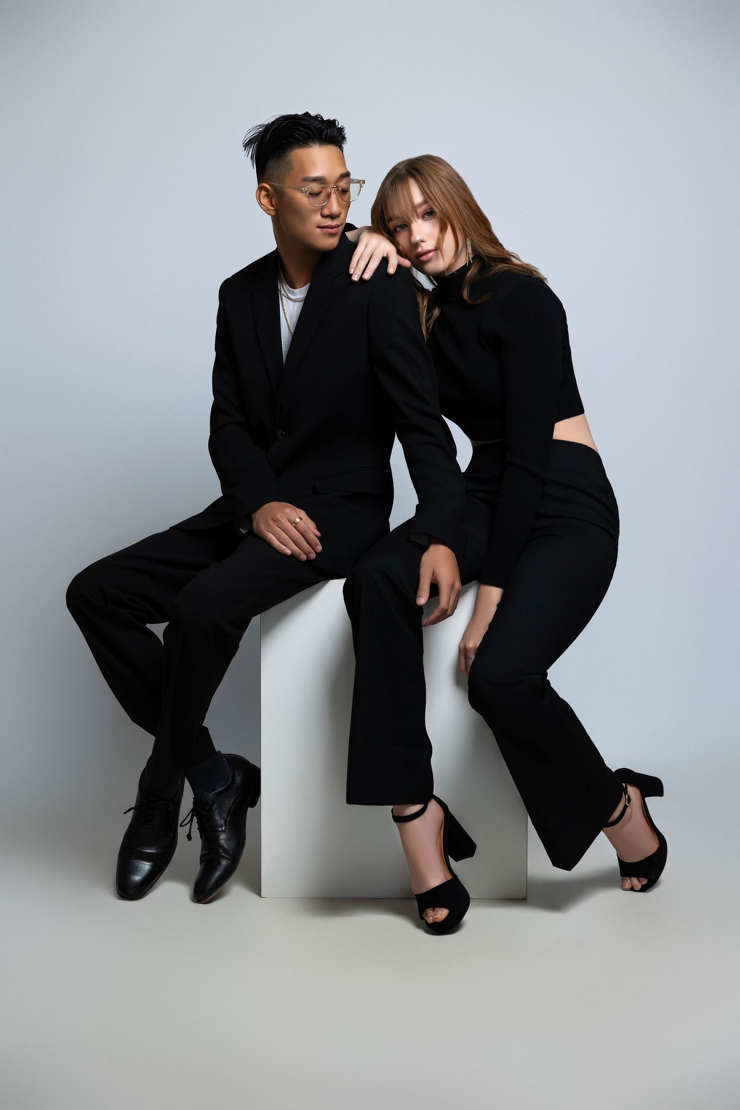 Stylish couple in matching black outfits pose together on white backdrop.