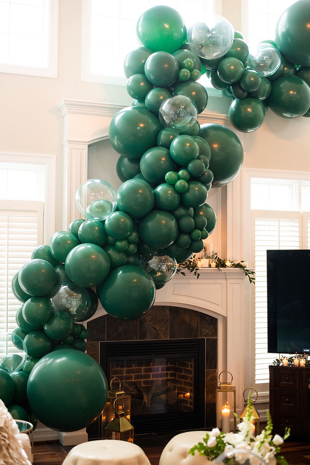 Green balloon garland with varying sizes of emerald and sage balloons decorates an elegant white fireplace mantel.