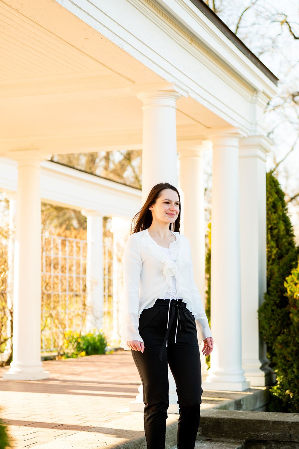 White columns and sunlit architecture create an elegant outdoor setting for a portrait captured in warm natural light.