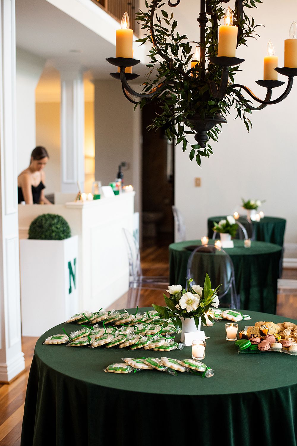 Elegant banquet setup with dark green tablecloths, decorative food displays, and ornate chandeliers in a bright event space.