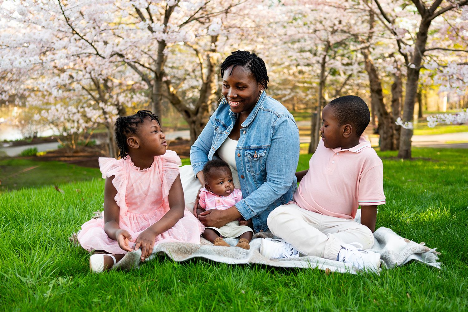 A group enjoys a sunny spring day together on a picturesque grassy lawn with pink blankets and joyful expressions.