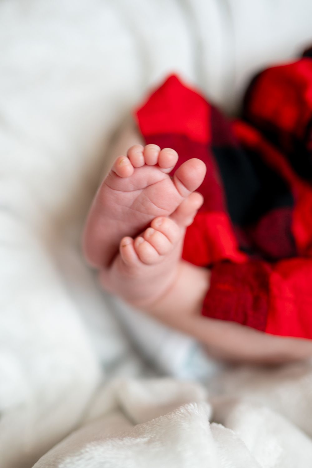 A tiny newborn baby's feet resting on soft white bedding with red fabric accent.