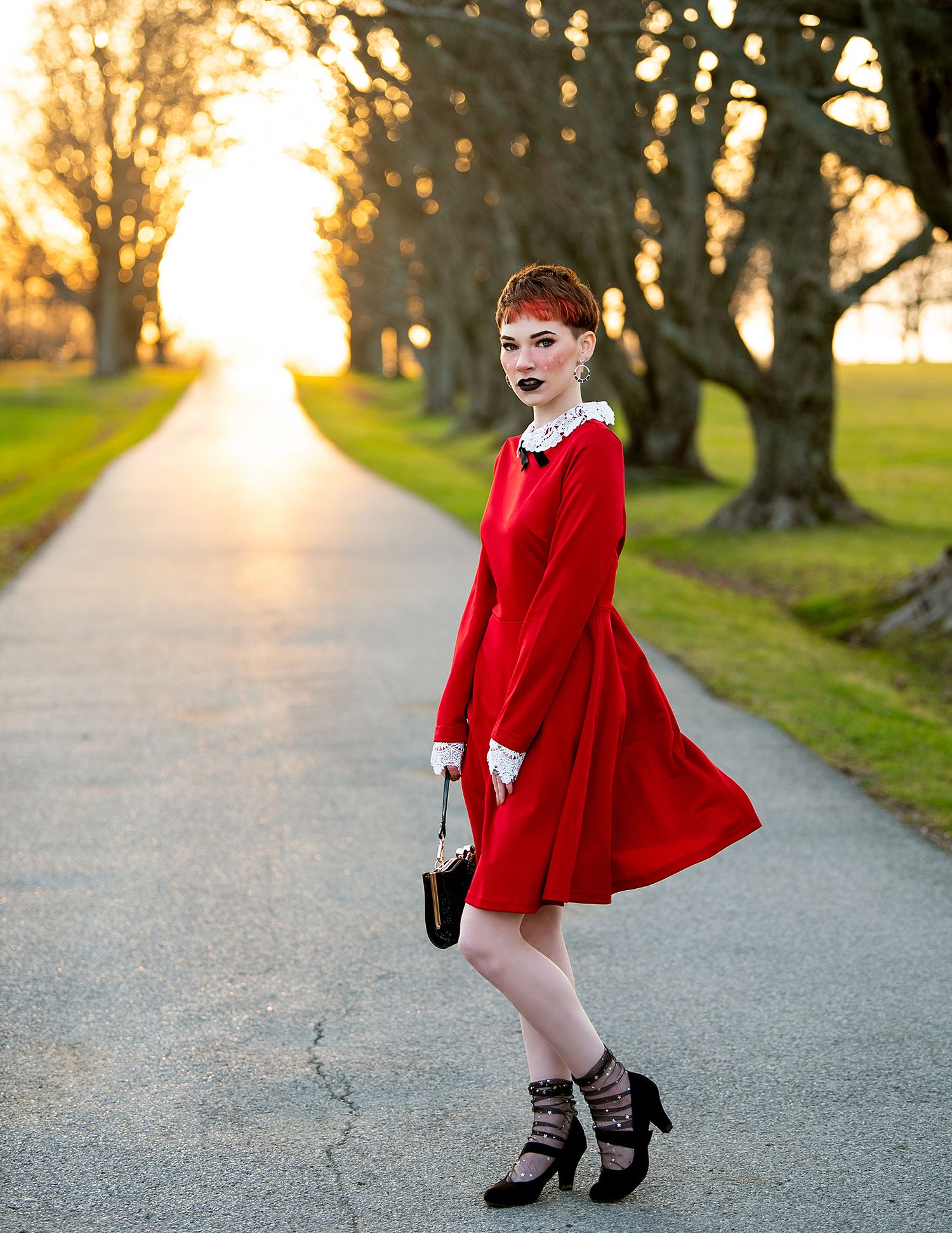 A retro-styled fashion photo on a tree-lined path at sunset featuring a bright red dress and heels.
